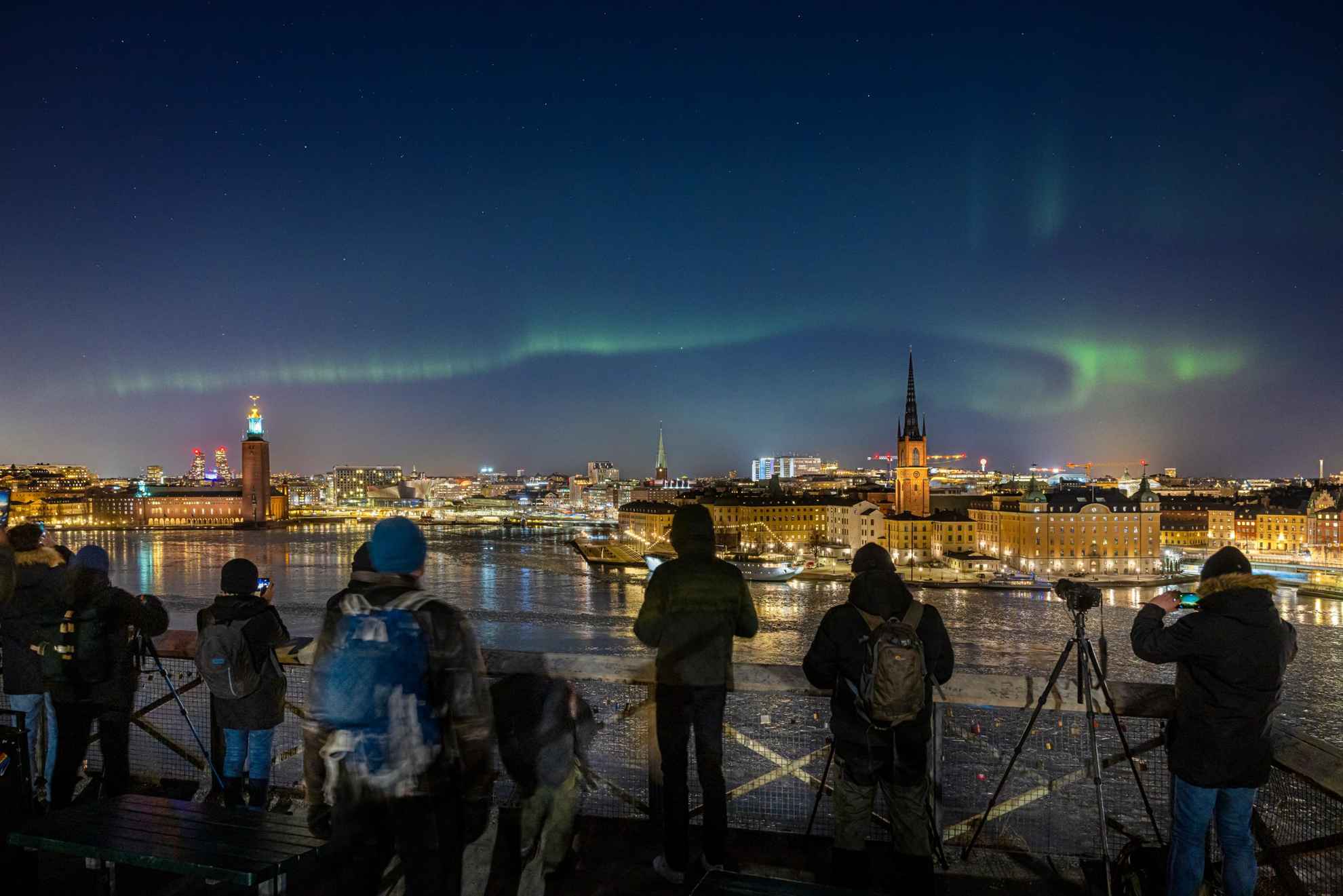 Northern lights over a city landscape, with photographers lined up to get a shot.
