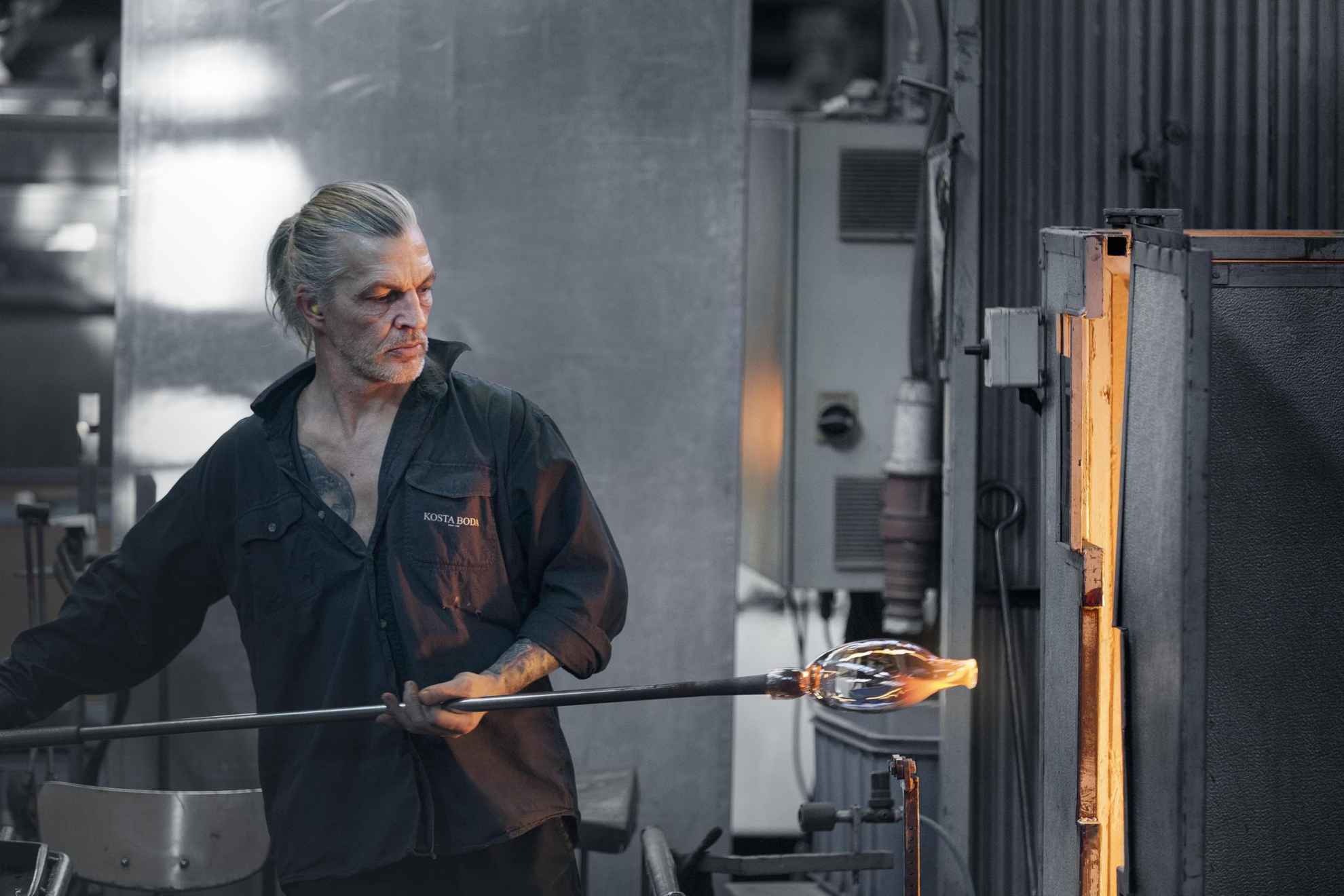 A glass blower working with hand-blown glass in a workshop.