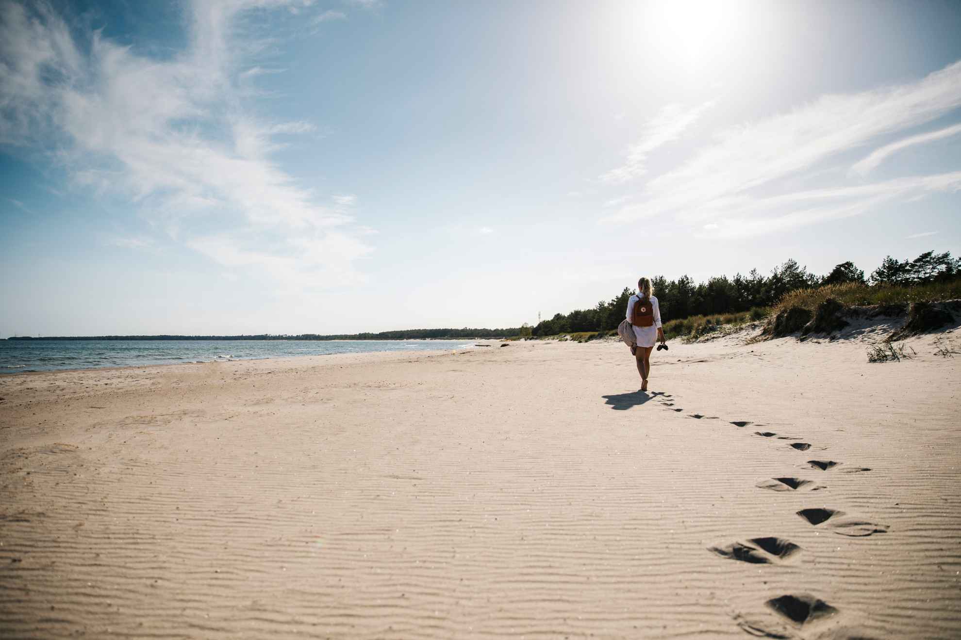Woman walking on a white beach on Öland with a backpack on her back and shoes in her hand