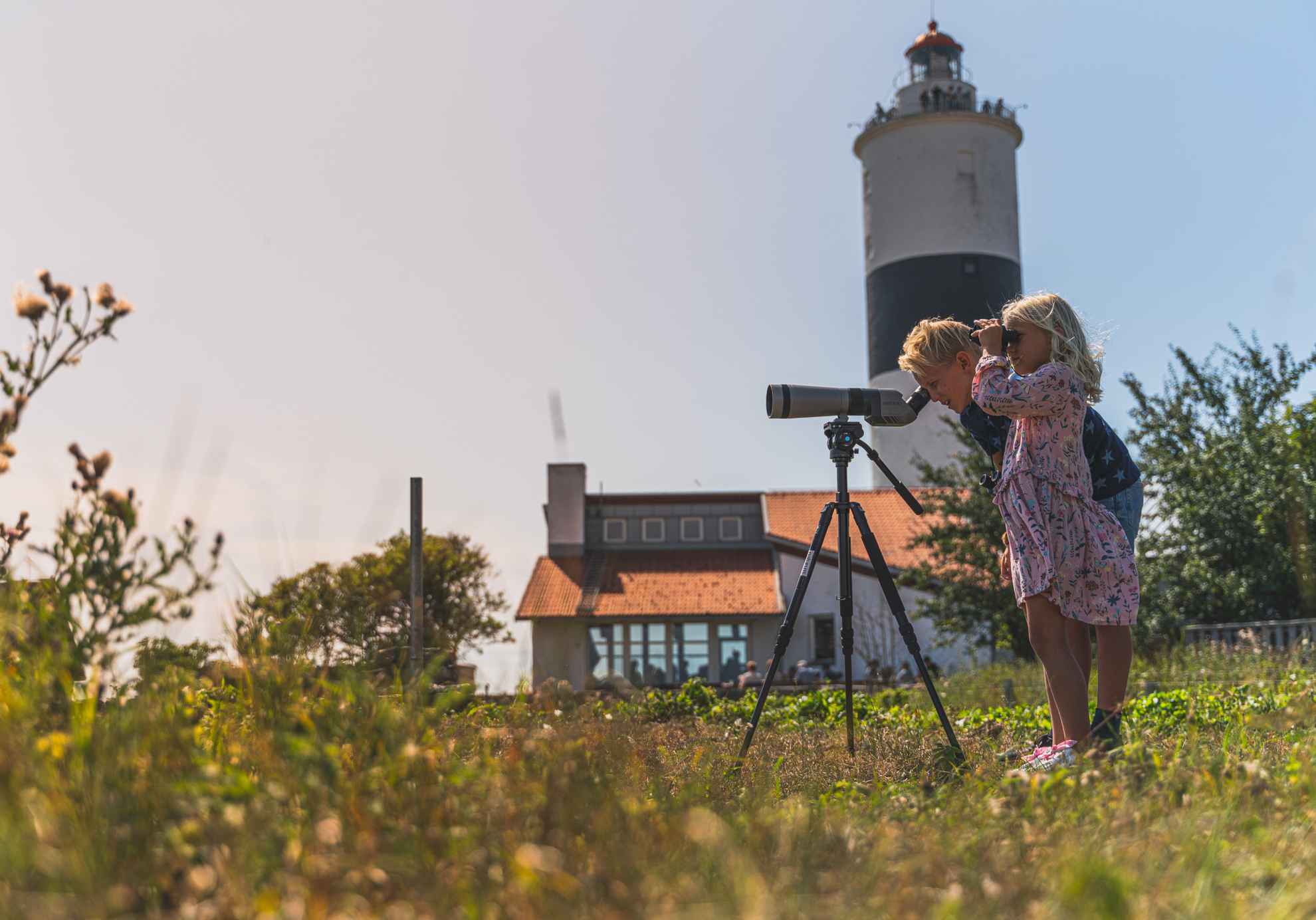 A girl and a boy looking at birds through a telescope by the lighthouse Långe Jan at Öland