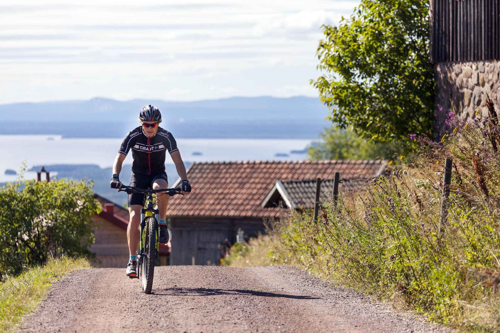 A biker in biking gear going up a hill, with wooden houses, hills and the sea in the background.