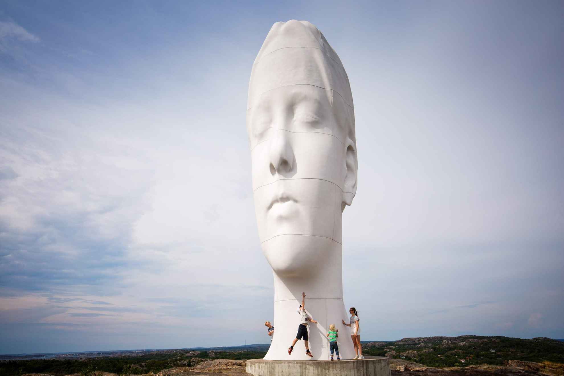 A large statue in the shape of a human head standing in the middle of nature, with four people standing standing right by it.