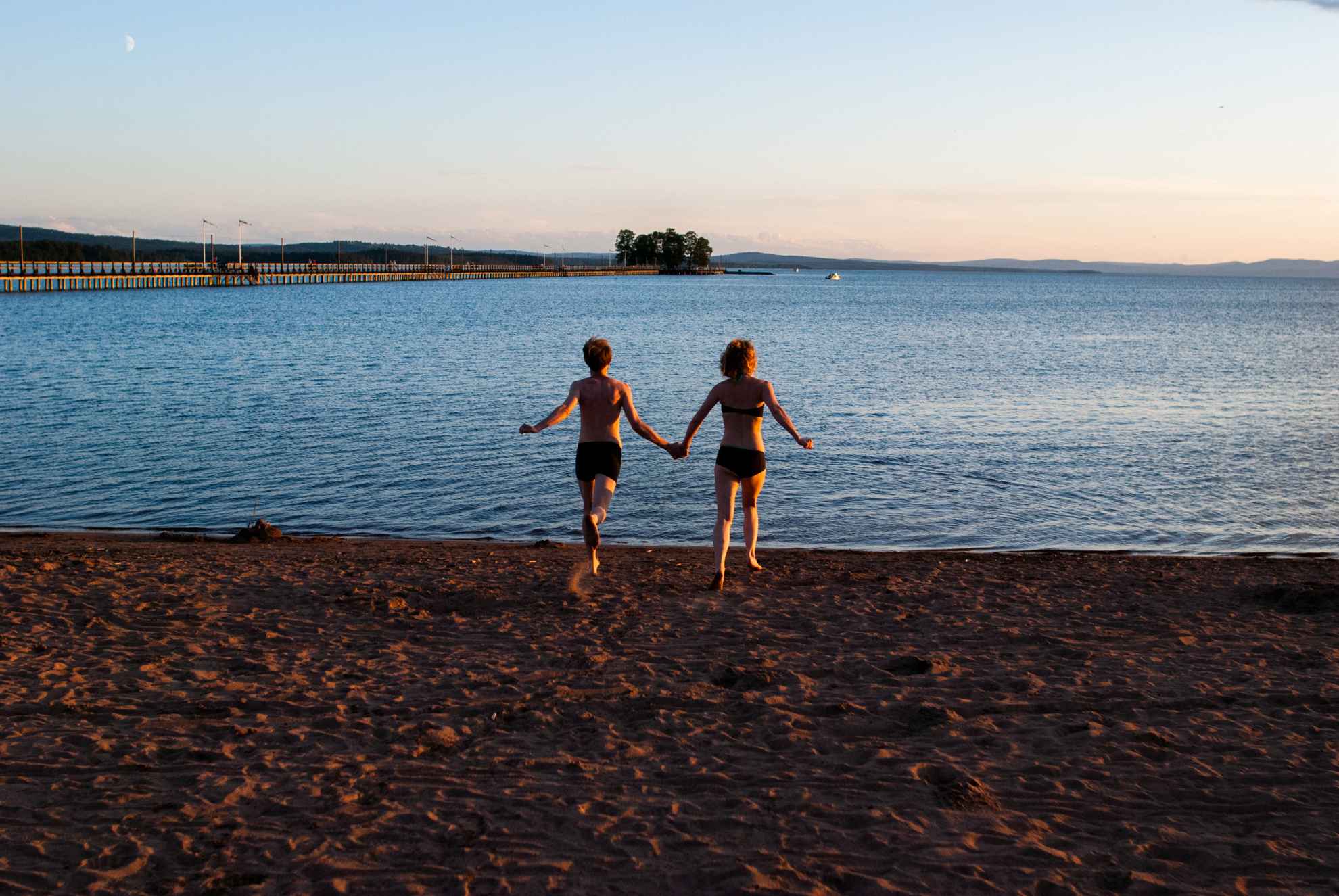Two people in bathing suits running on a beach towards the water.