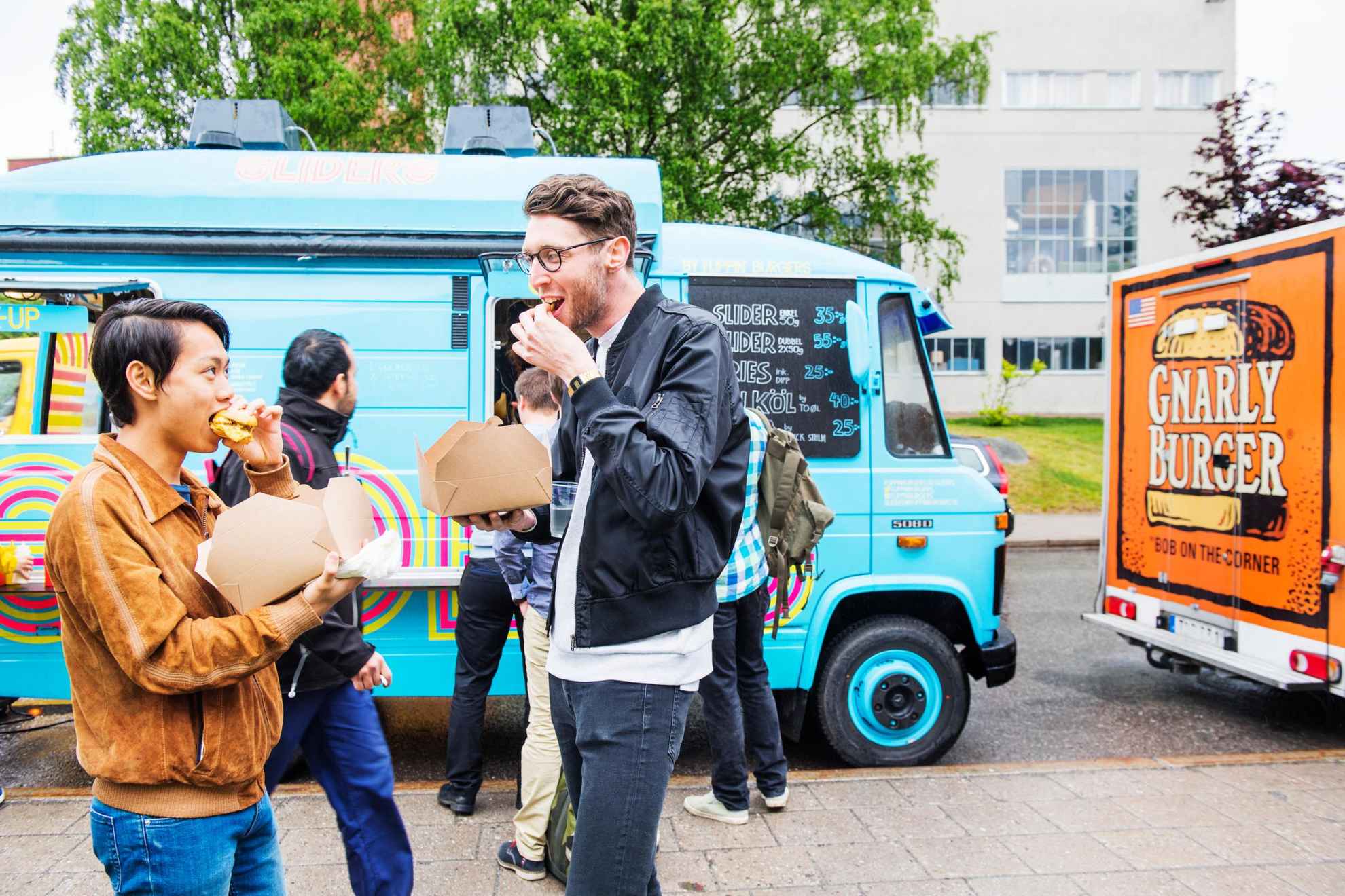 Friends are eating finger food out of boxes by a food truck parked in Stockholm.