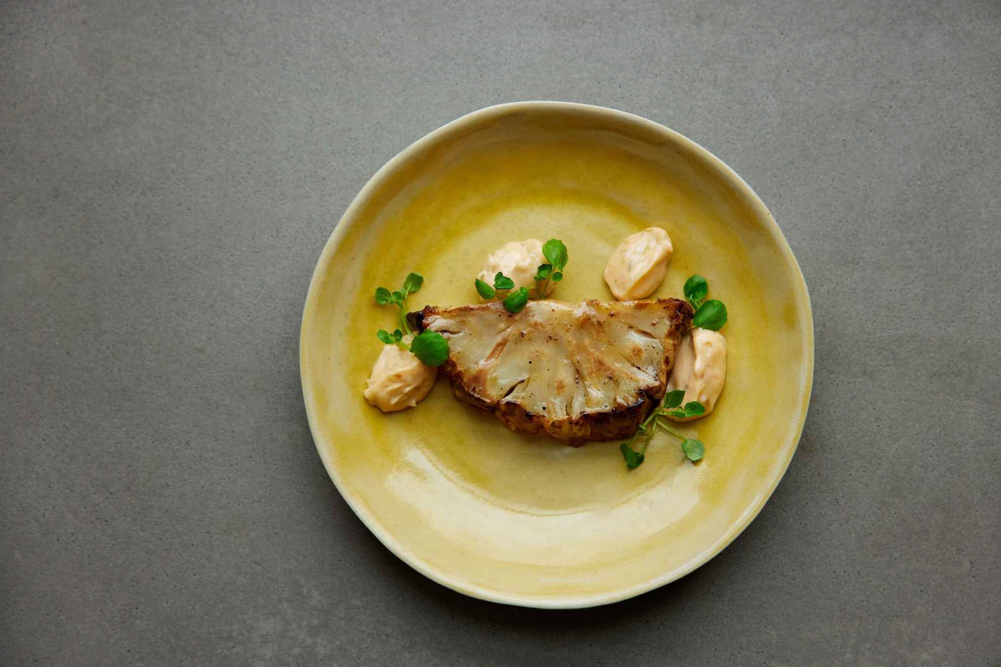 A yellow plate with a piece of baked cauliflower.