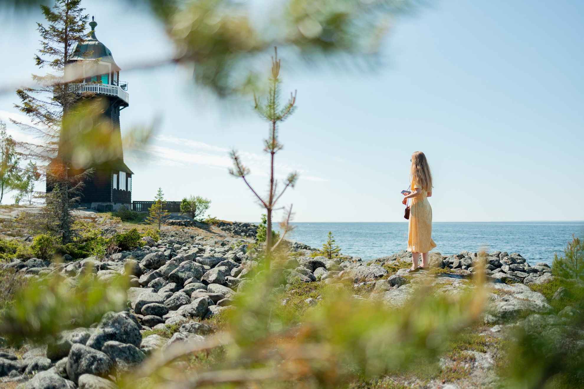 A woman is standing on a shore looking towards a lighthouse.