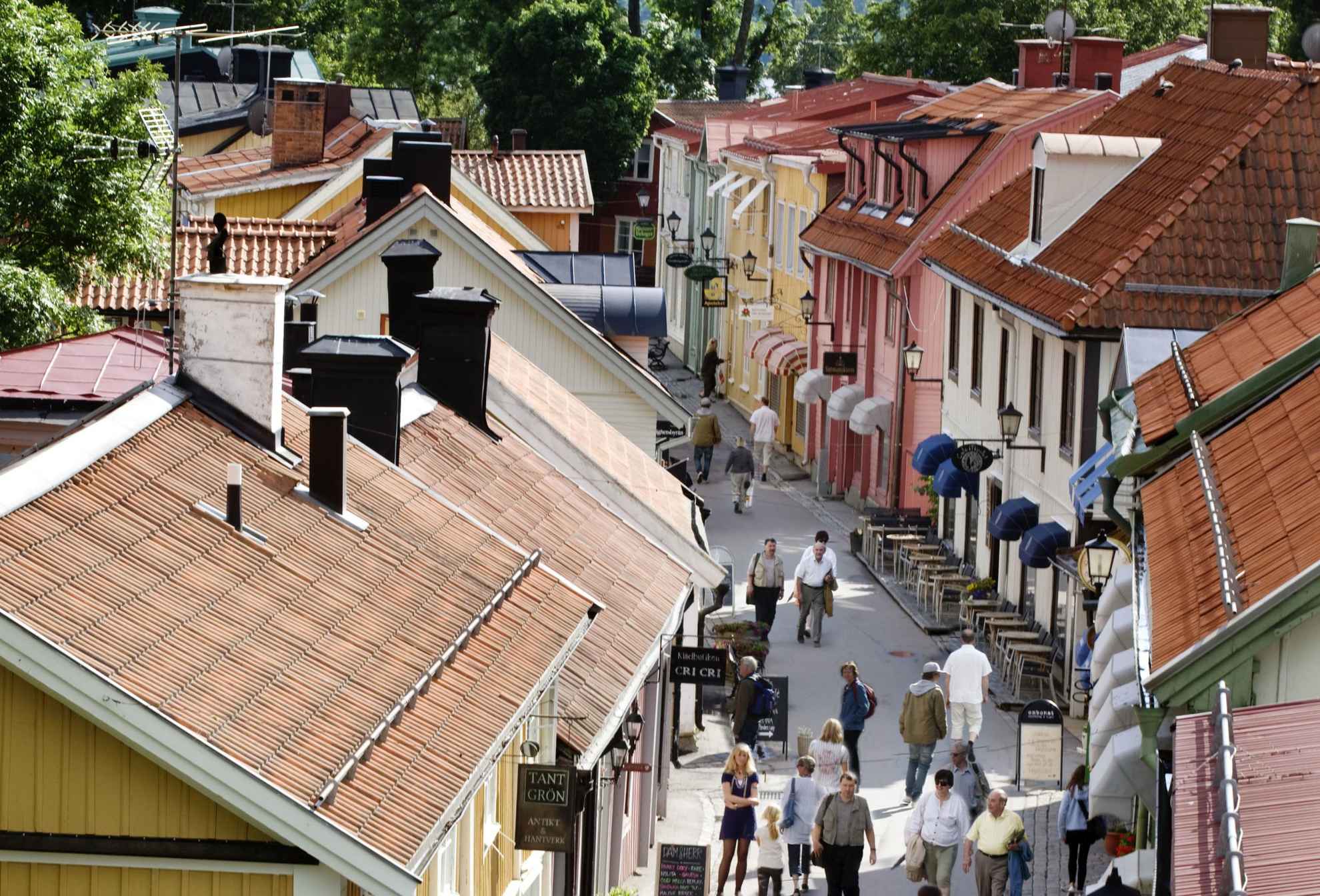 Wooden houses in different colours on a narrow street in Sigtuna, people walking on the street.