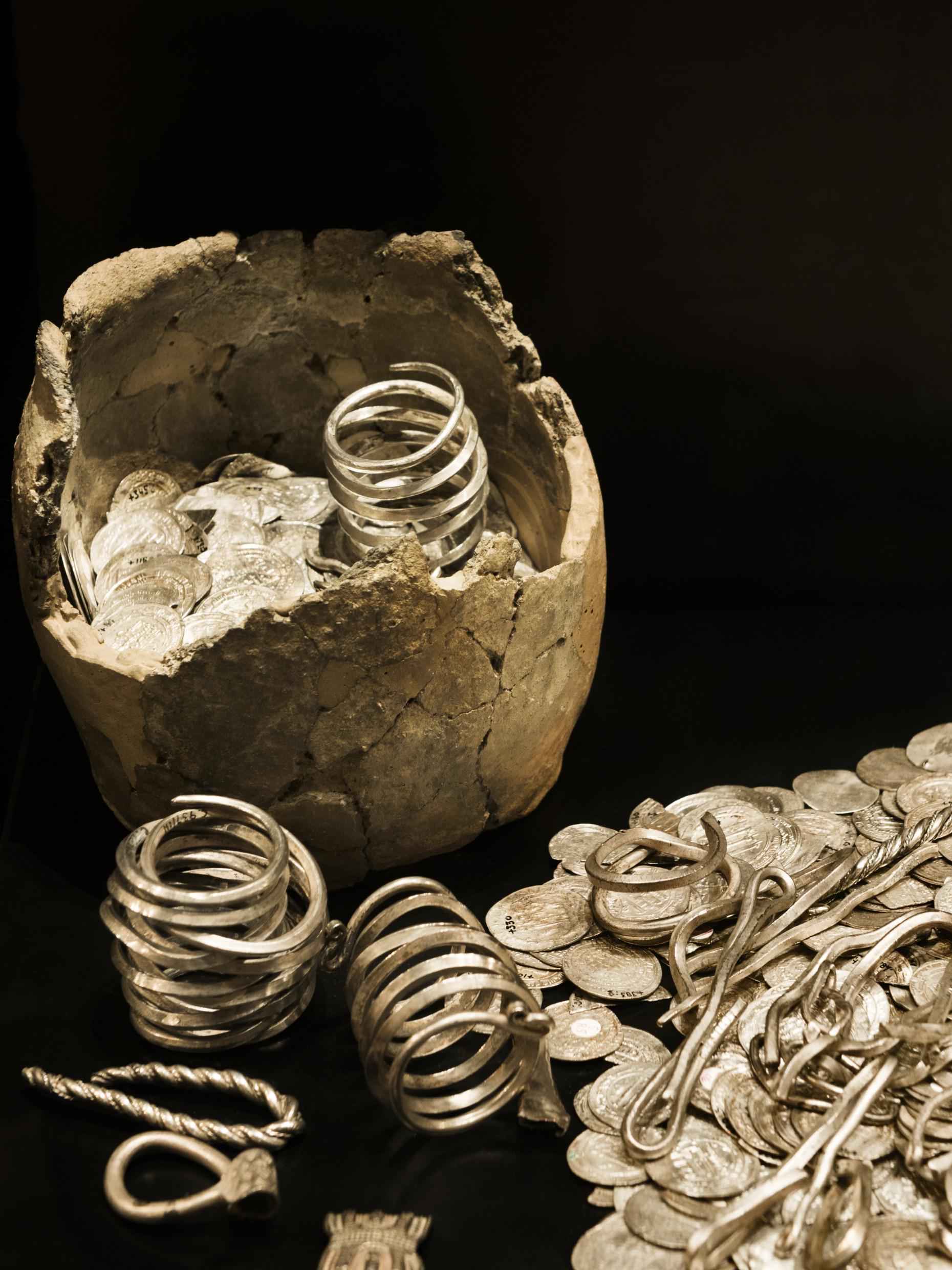Old silver and gold coins and jewelry on a black surface.