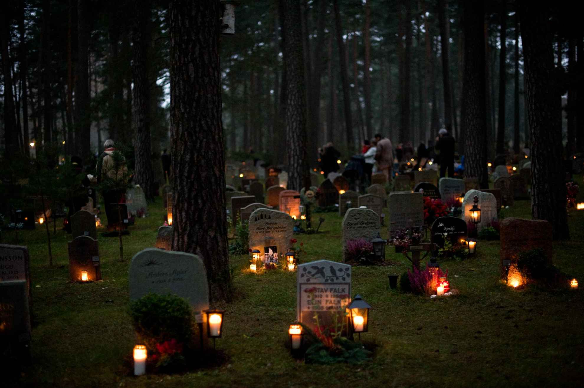 A graveyard in the forest with gravestones in the dark with candles and lanterns lit next to them.