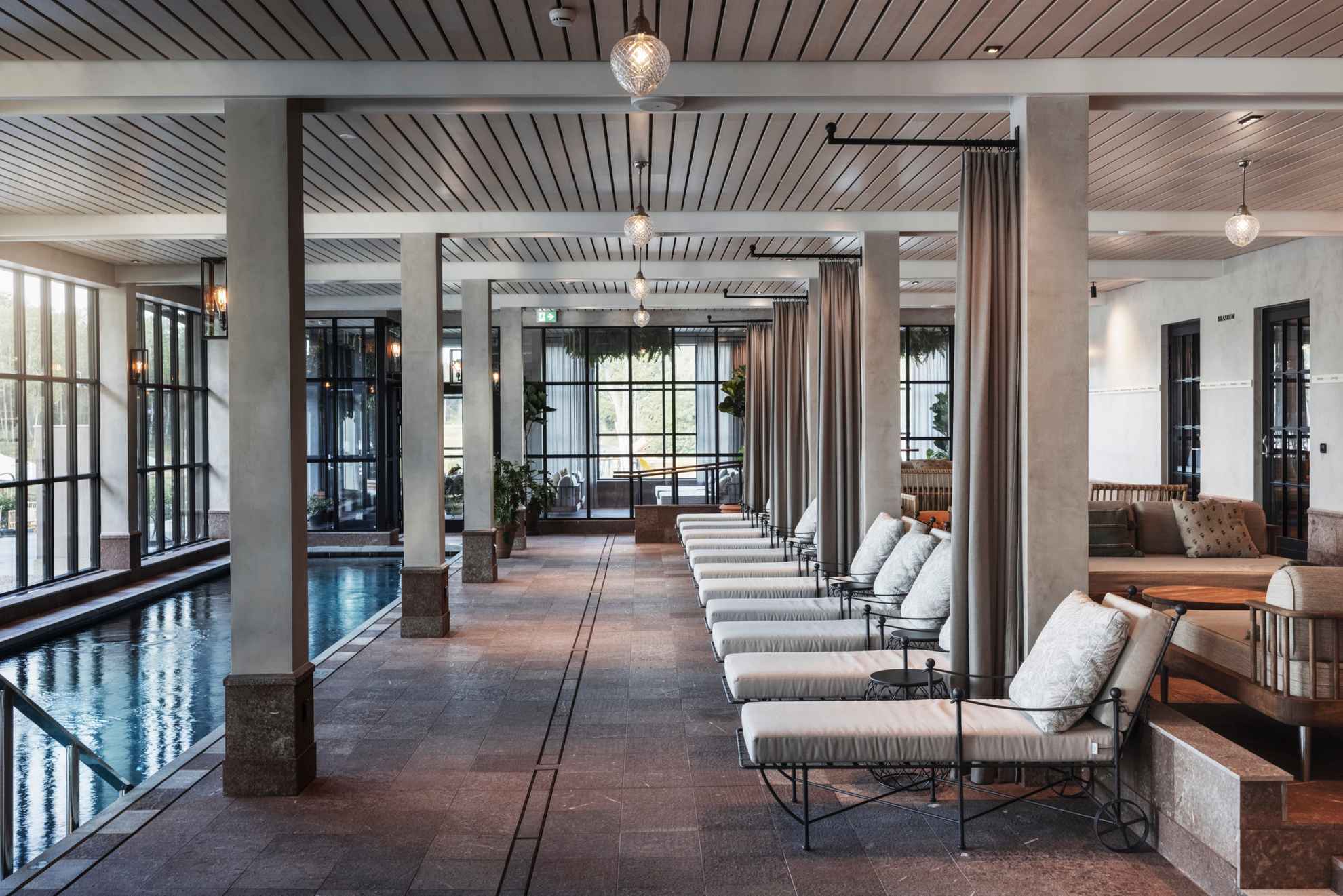 Lounge chairs, sofas and tables next to an indoor pool in the spa of Smådalarö Gård