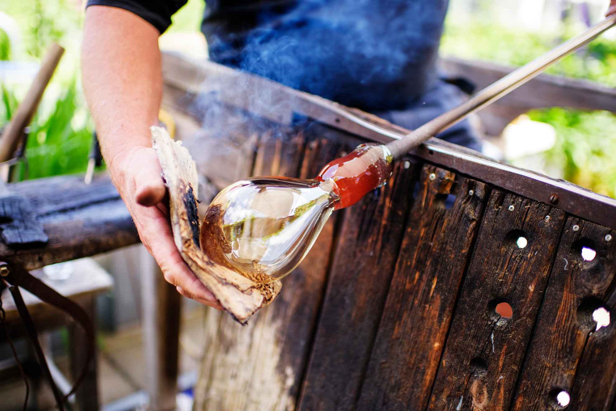 A man in the process of making hand-blown glass outdoors.