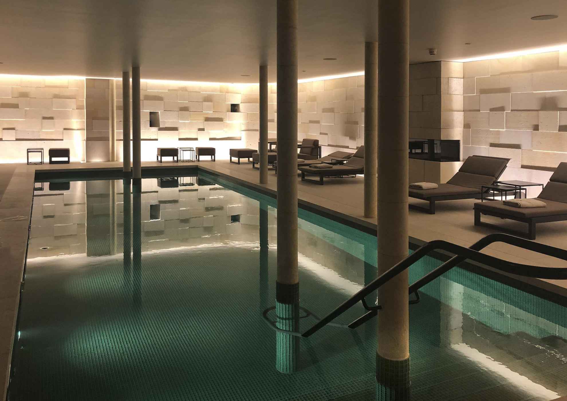 A dim lit room with lounge chairs and an indoor pool.