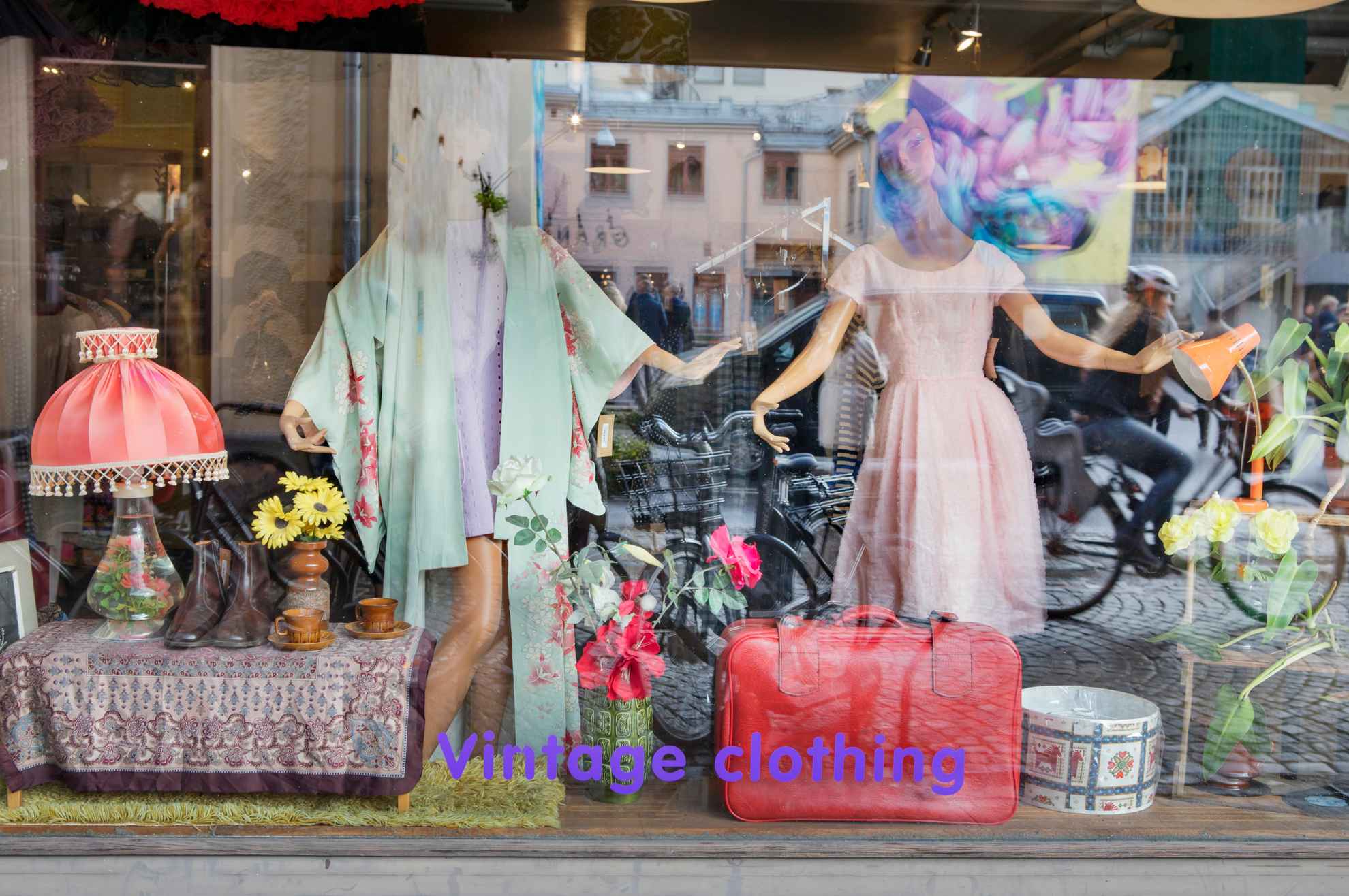 A shop window with vintage clothing. You can see reflections in the window of people moving.