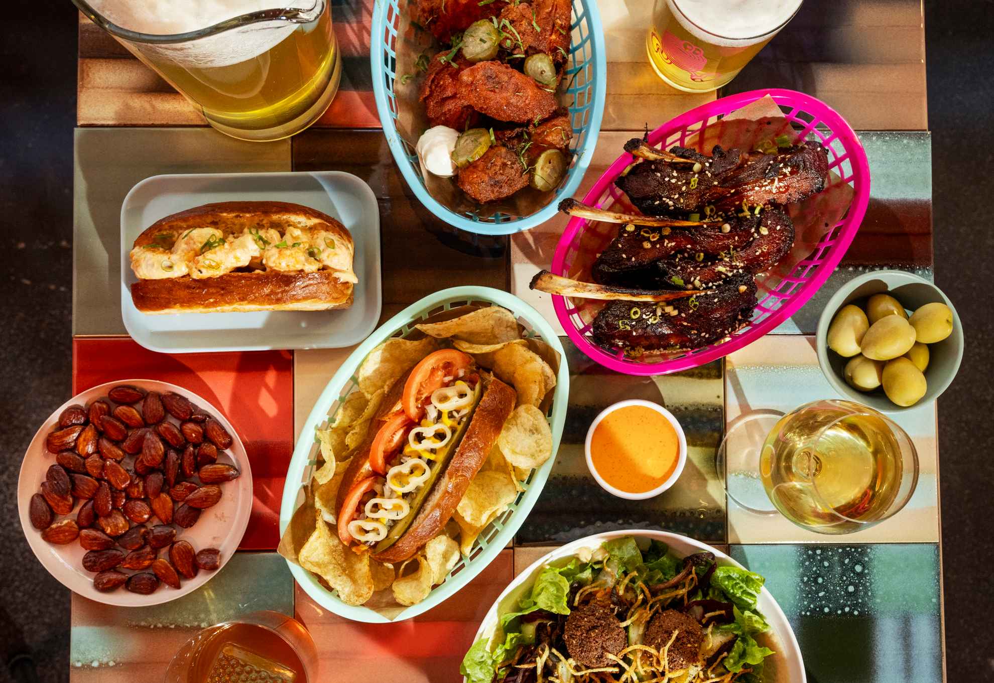 A square table filled with colourful streetfood in different baskets and on plates, as well as glasses of beer and wine.