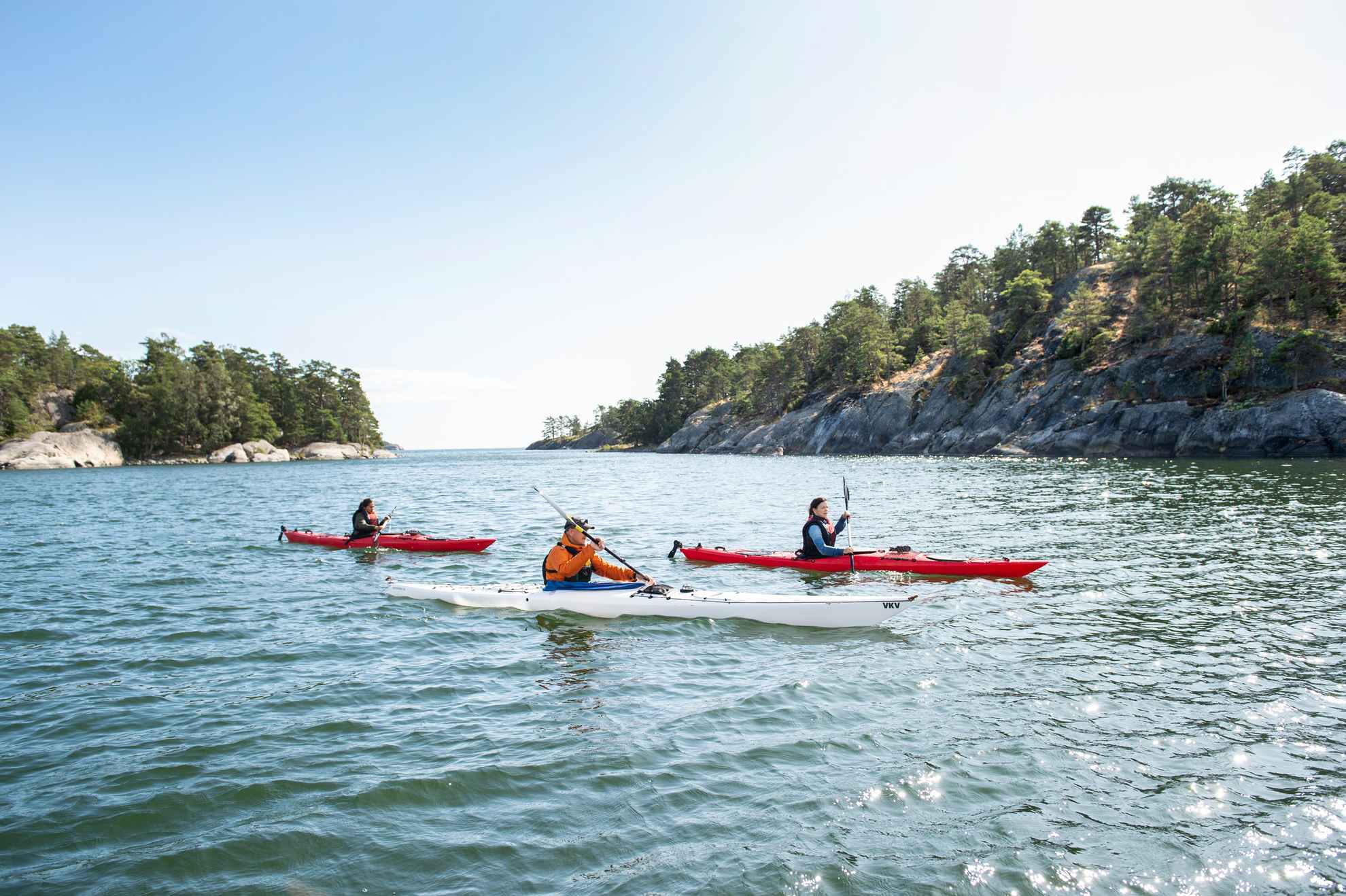 Three persons kayaking between islets in the archipelago.