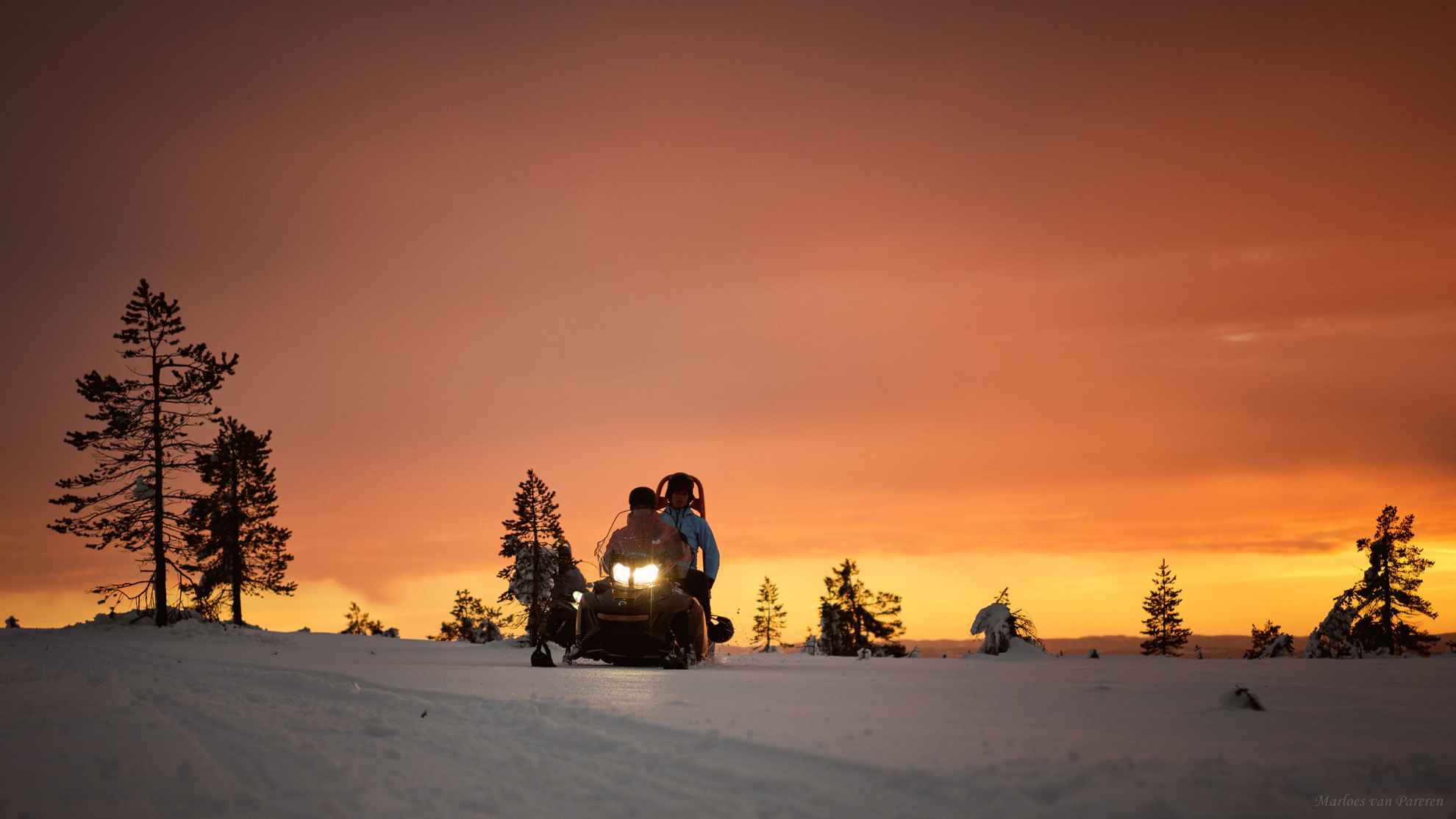 Two people on a snowmobile during the evening.