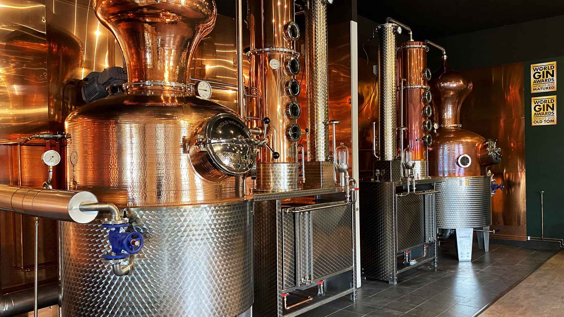 Two hand hammered copper stills in front of a shiny copper wall in a distillery.