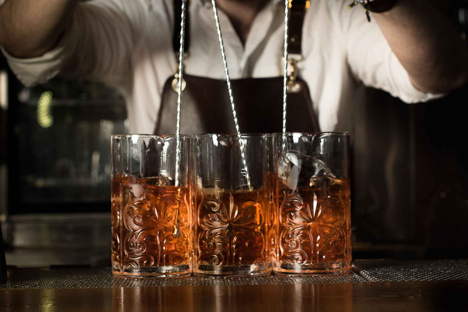 A close-up of three drinks being stirred by a bartender.