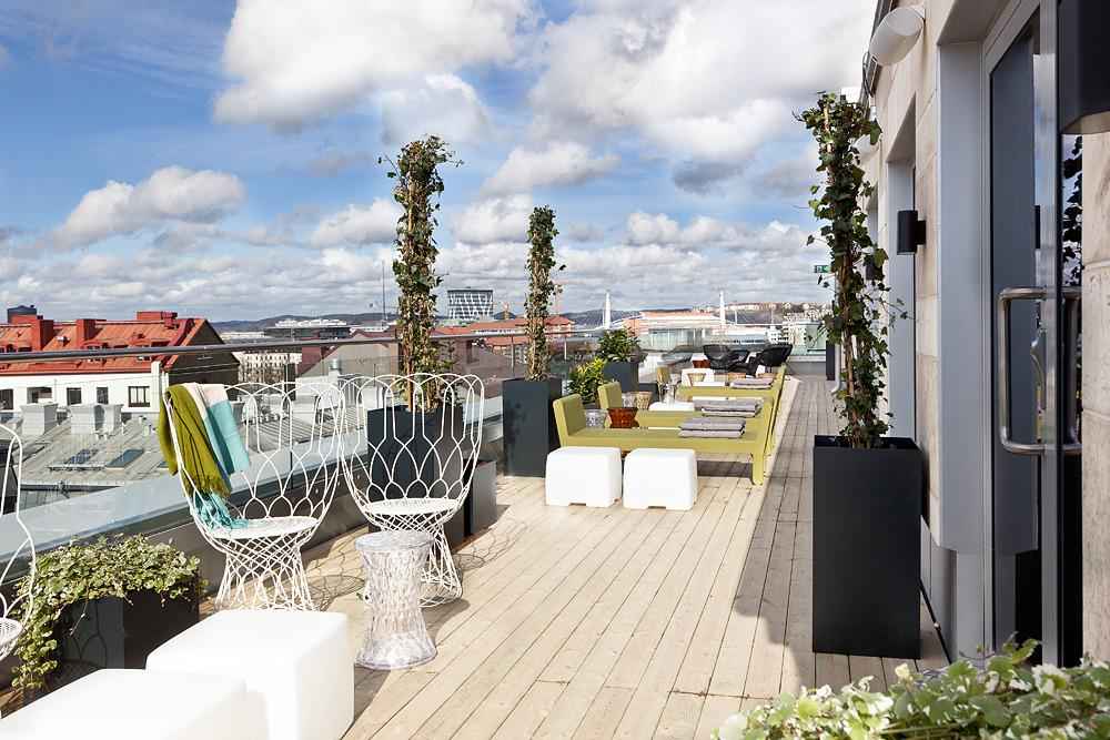 A rooftop with wooden floor and white and yellow furniture..