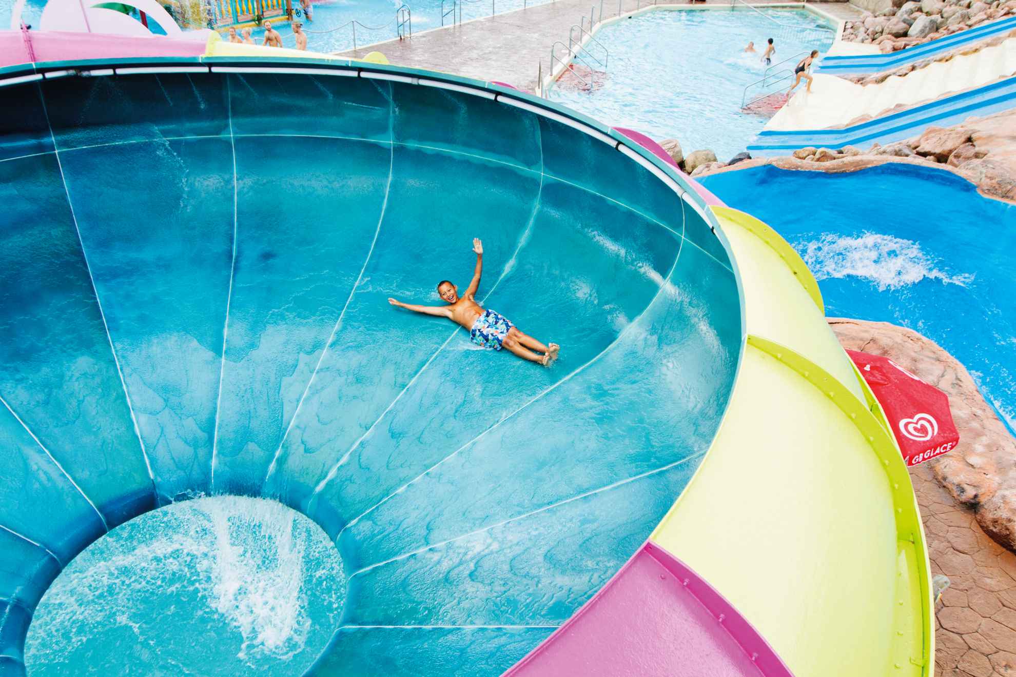 Young boy riding a colorful water slide at Skara Sommarland with the pool area in the background