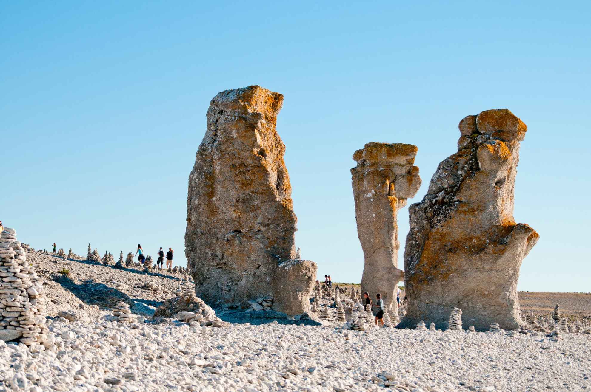 Limestone monoliths on a rocky beach on Gotland, with a few people walking in the background.