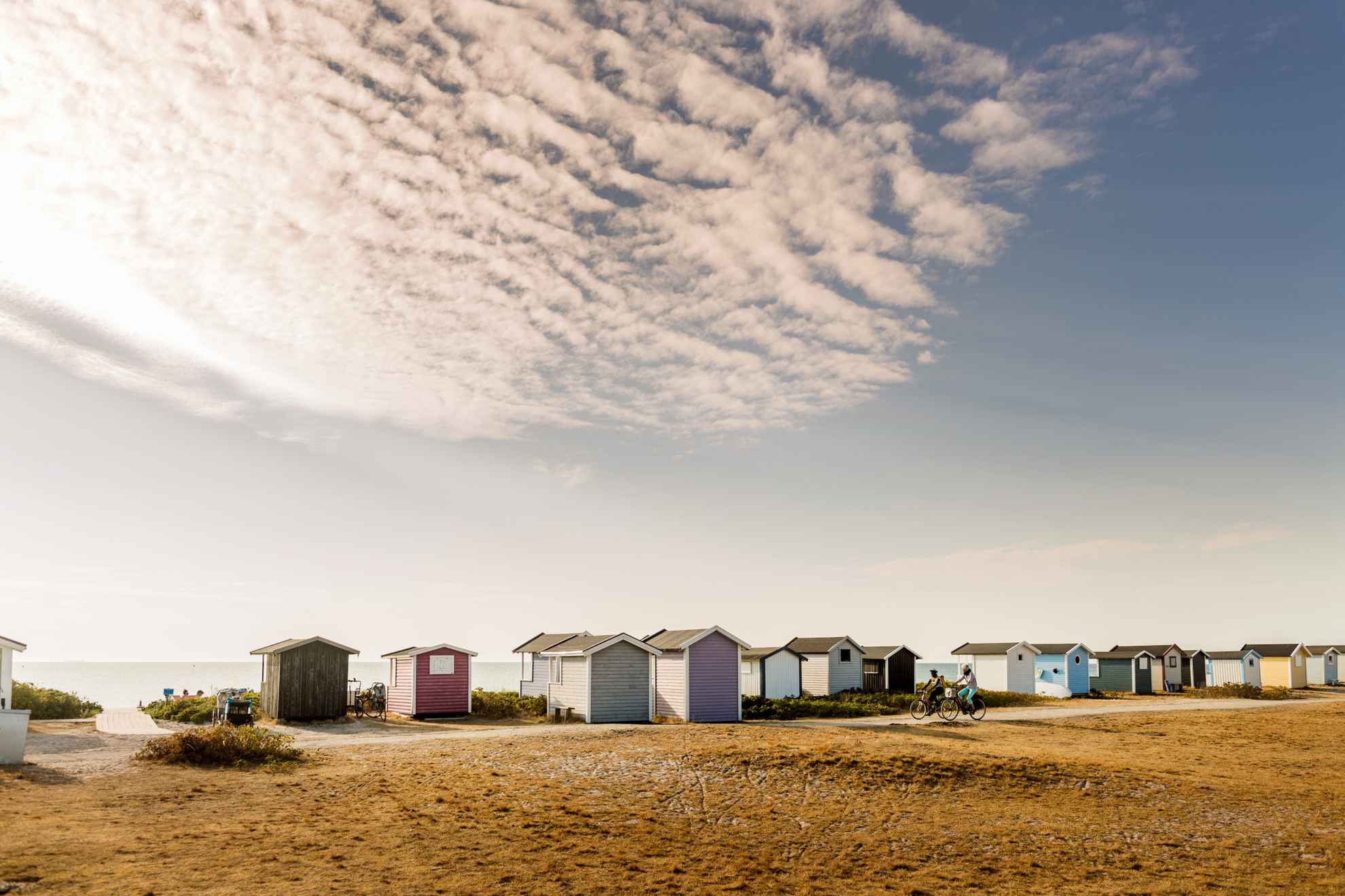 The back of colourful boathouses lined up on the beach. The sea is visible in the background.