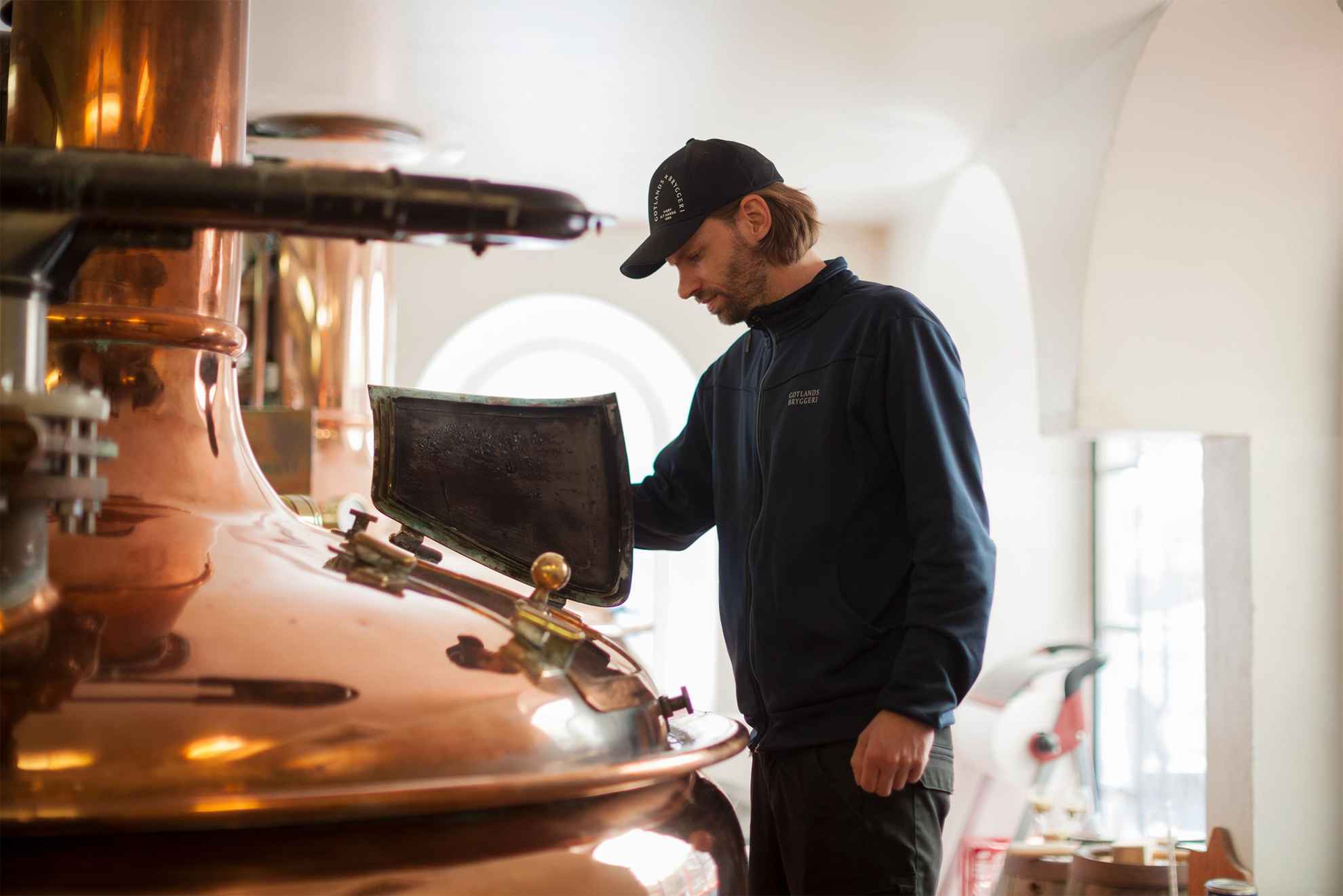 An employee at Gotlands Bryggeri is looking inside a copper boiler at the brewery.