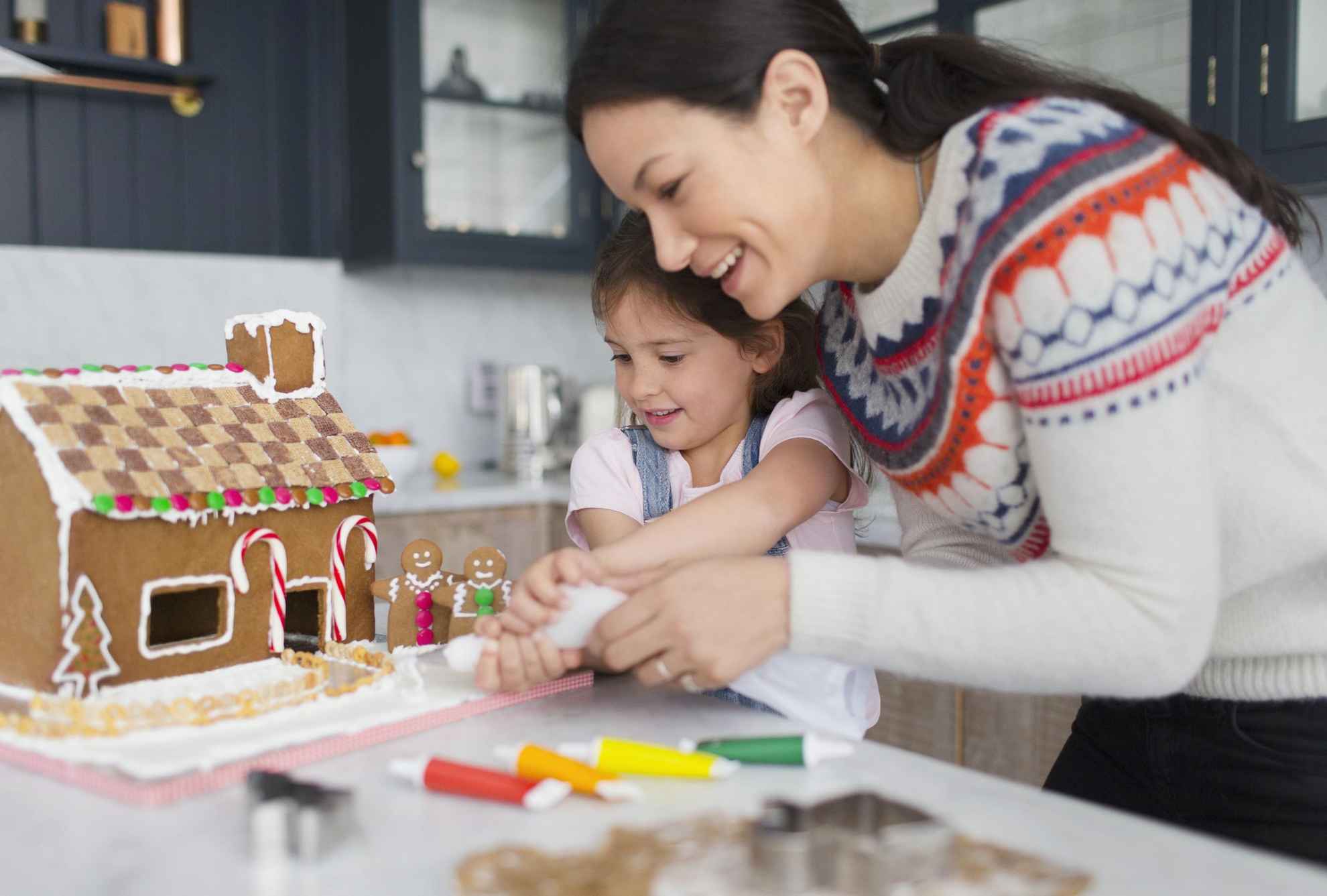 A woman and a child are making a gingerbread house.