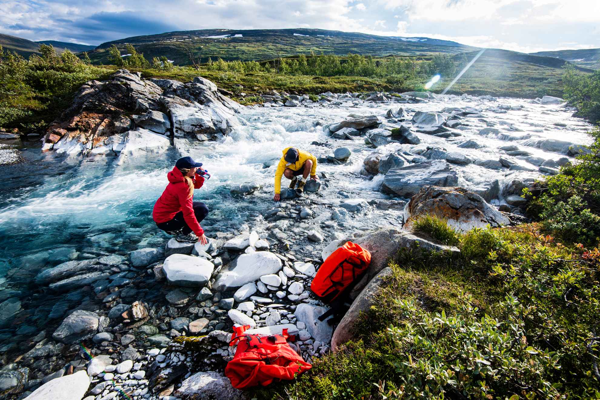 Two people are drinking from a river in Swedish Lapland.