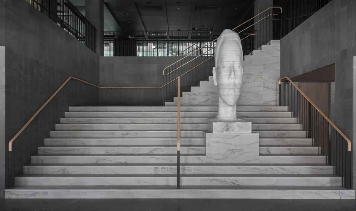 A marble sculpture of a human head is standing on a marble staircase.
