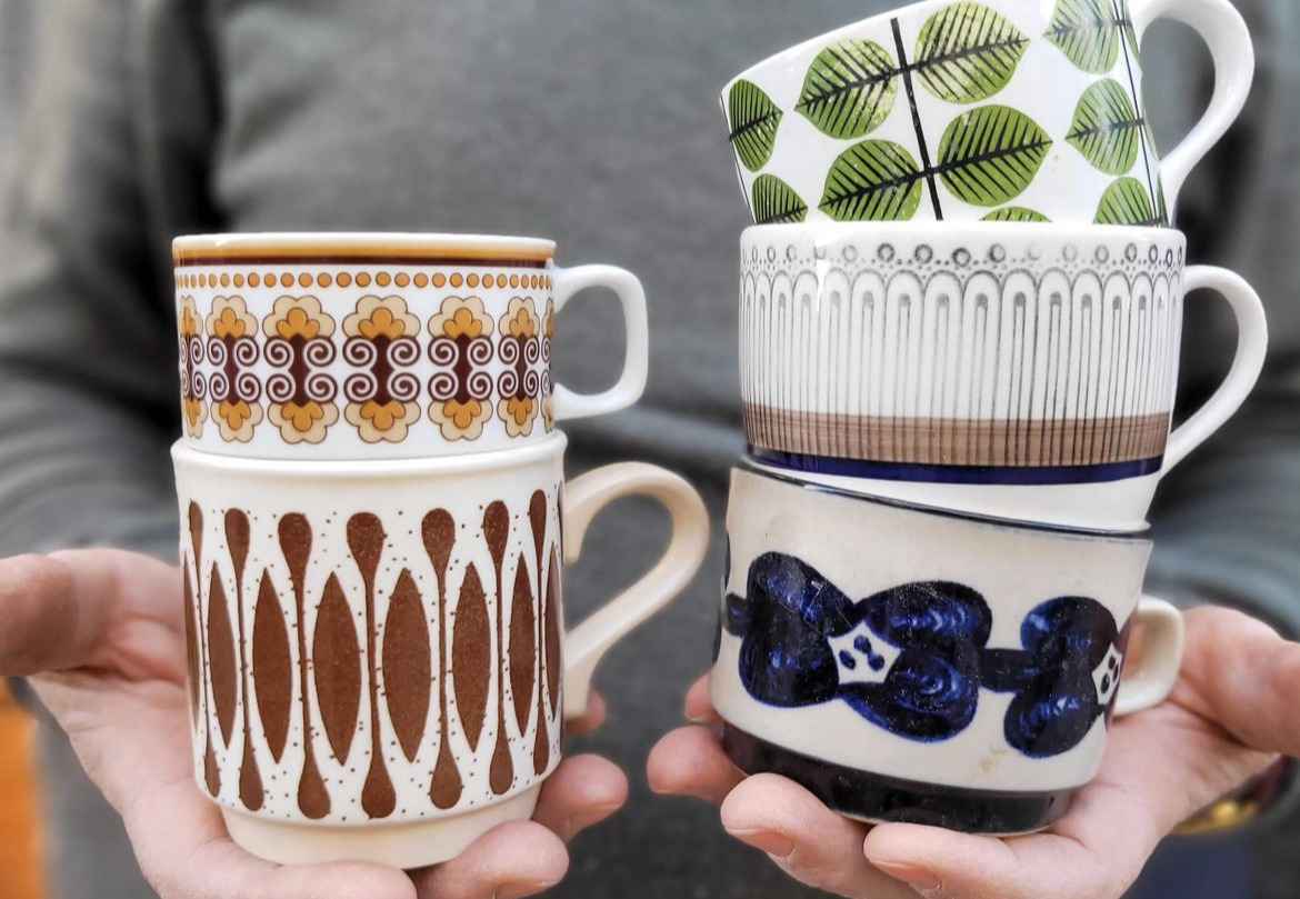 Hands holding five second-hand mugs with different patterns.