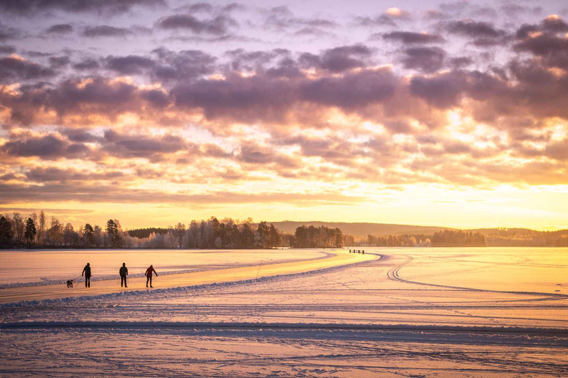 Silhouette of three people skating on a frozen lake. The sun is shining orange.