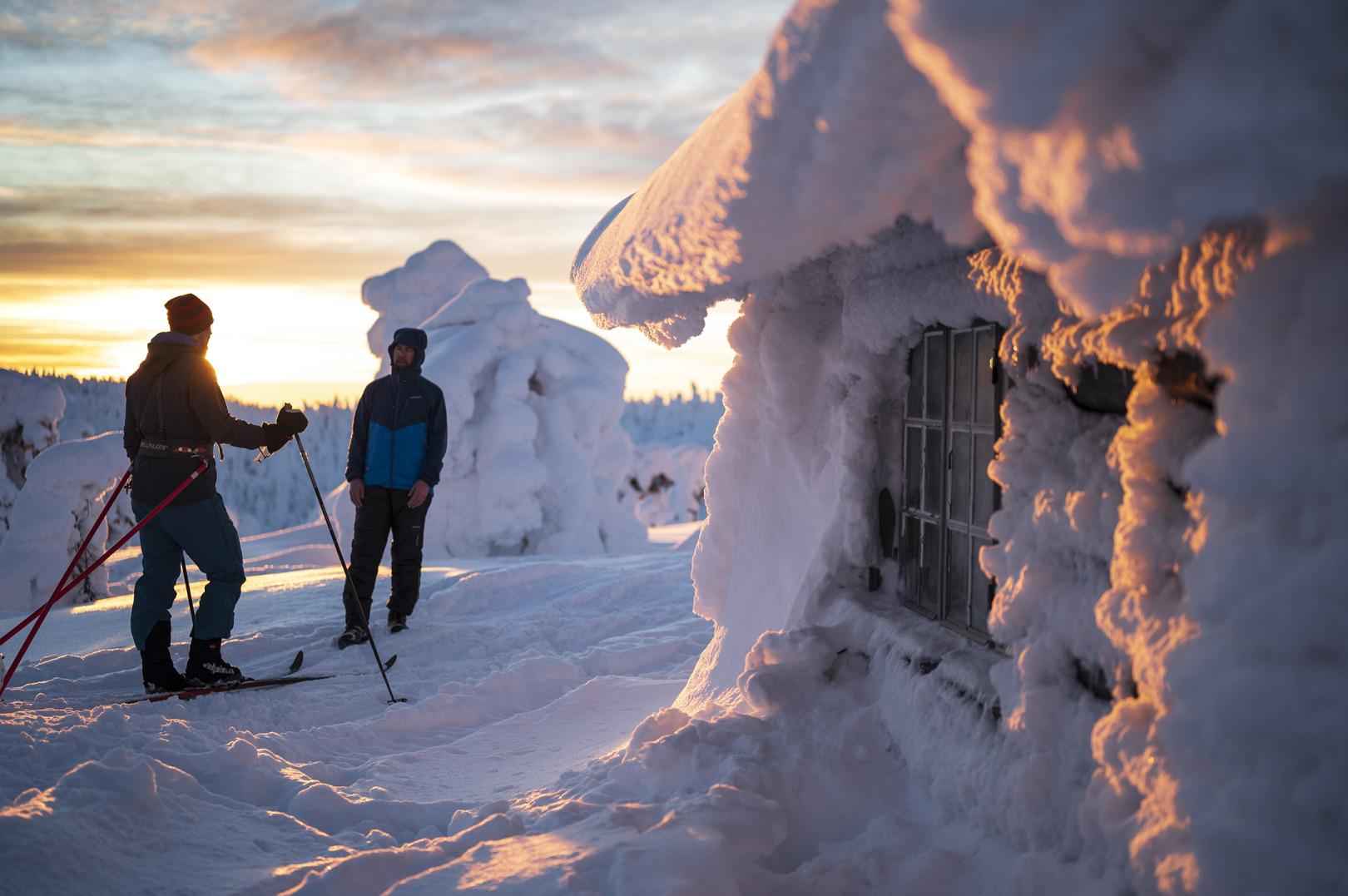 Ski-tourers by a cottage in winter landscape.