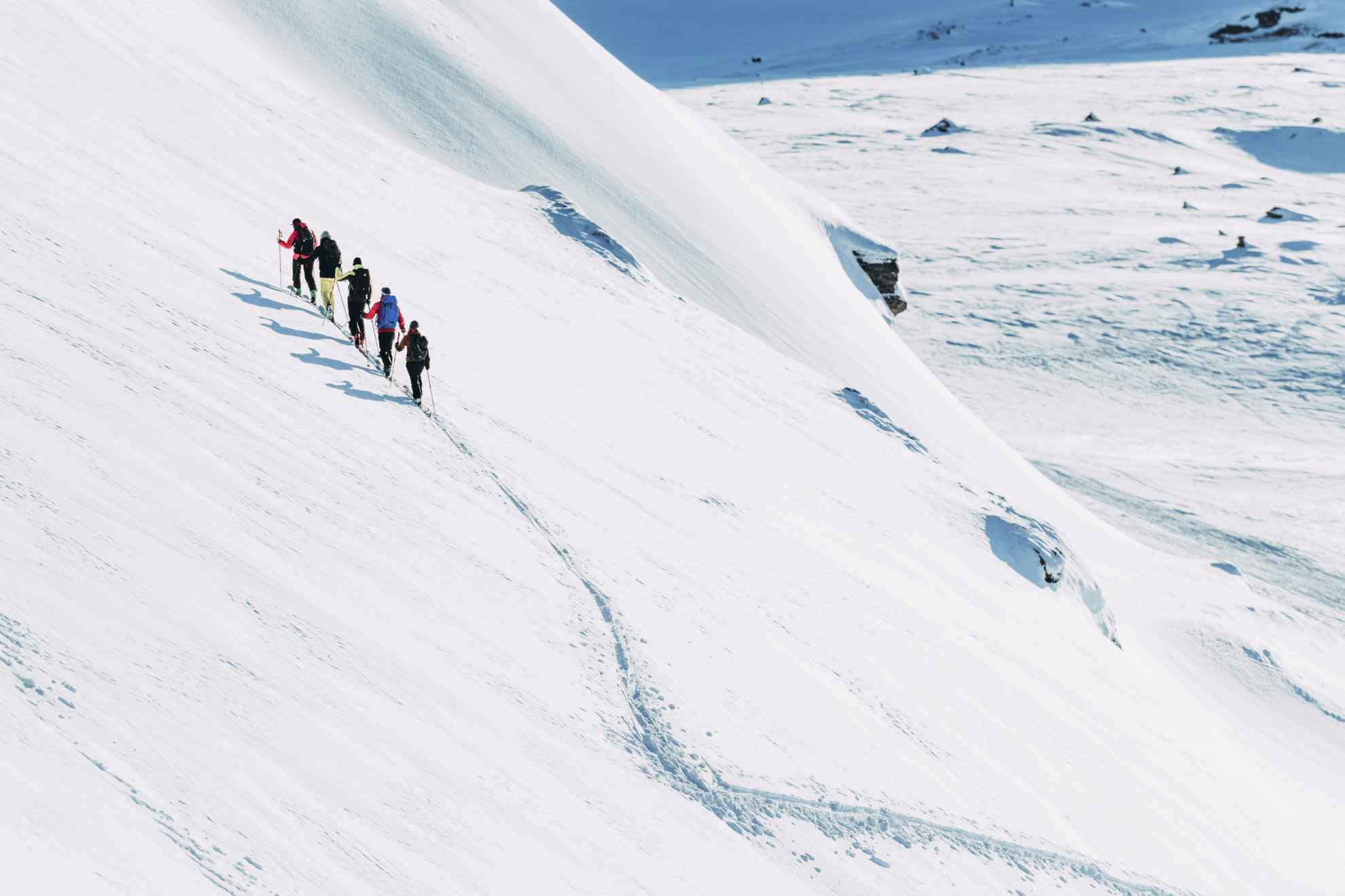 Five people with skis are on their way up a snow-covered mountain.
