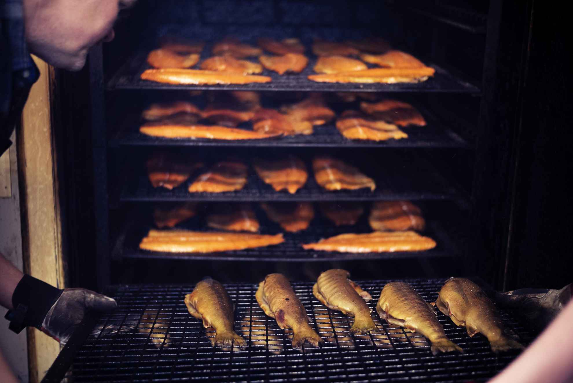 A plate of char and rainbow trout is placed in the smoker.