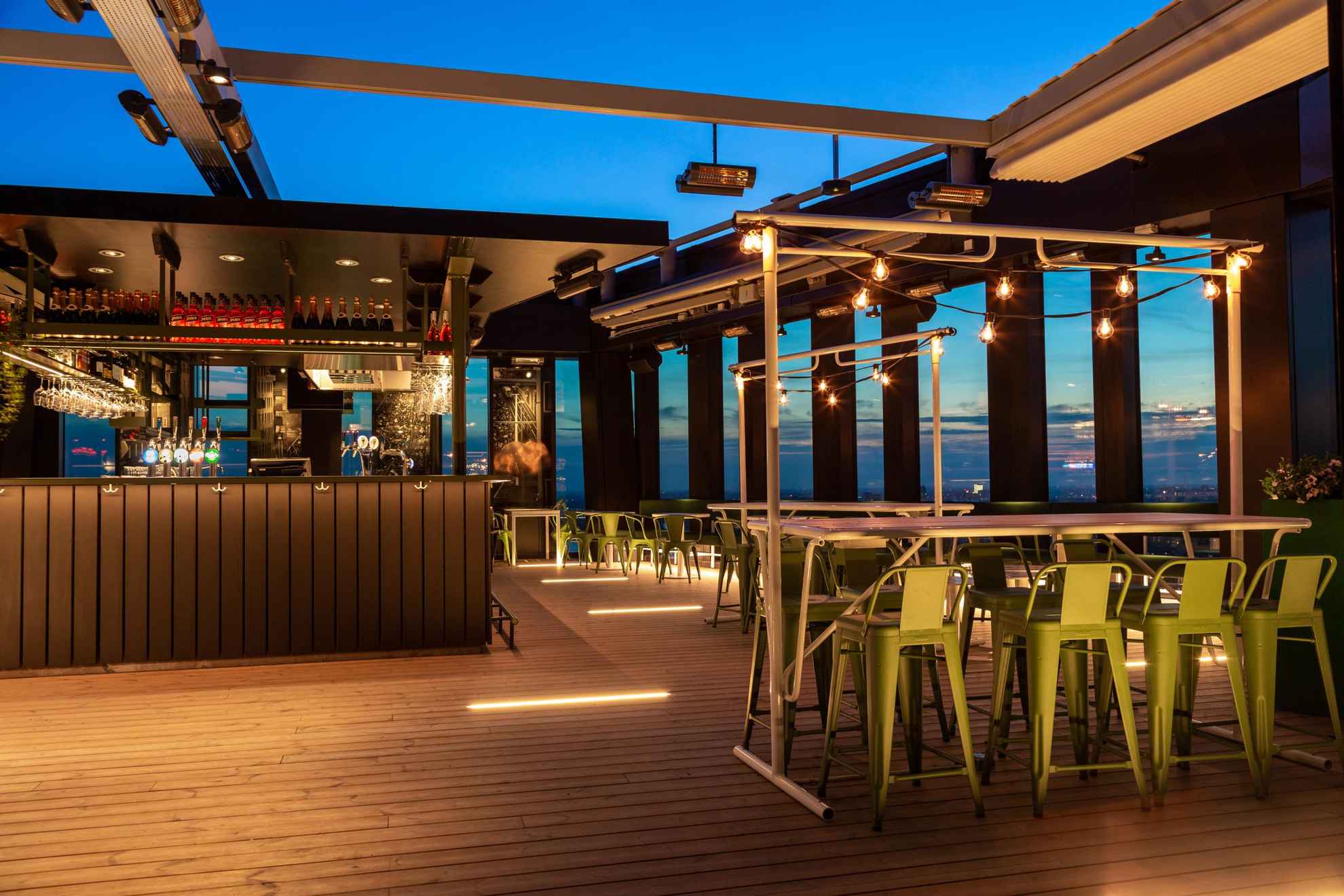 A rooftop bar with a seats and tables on a wooden floor.