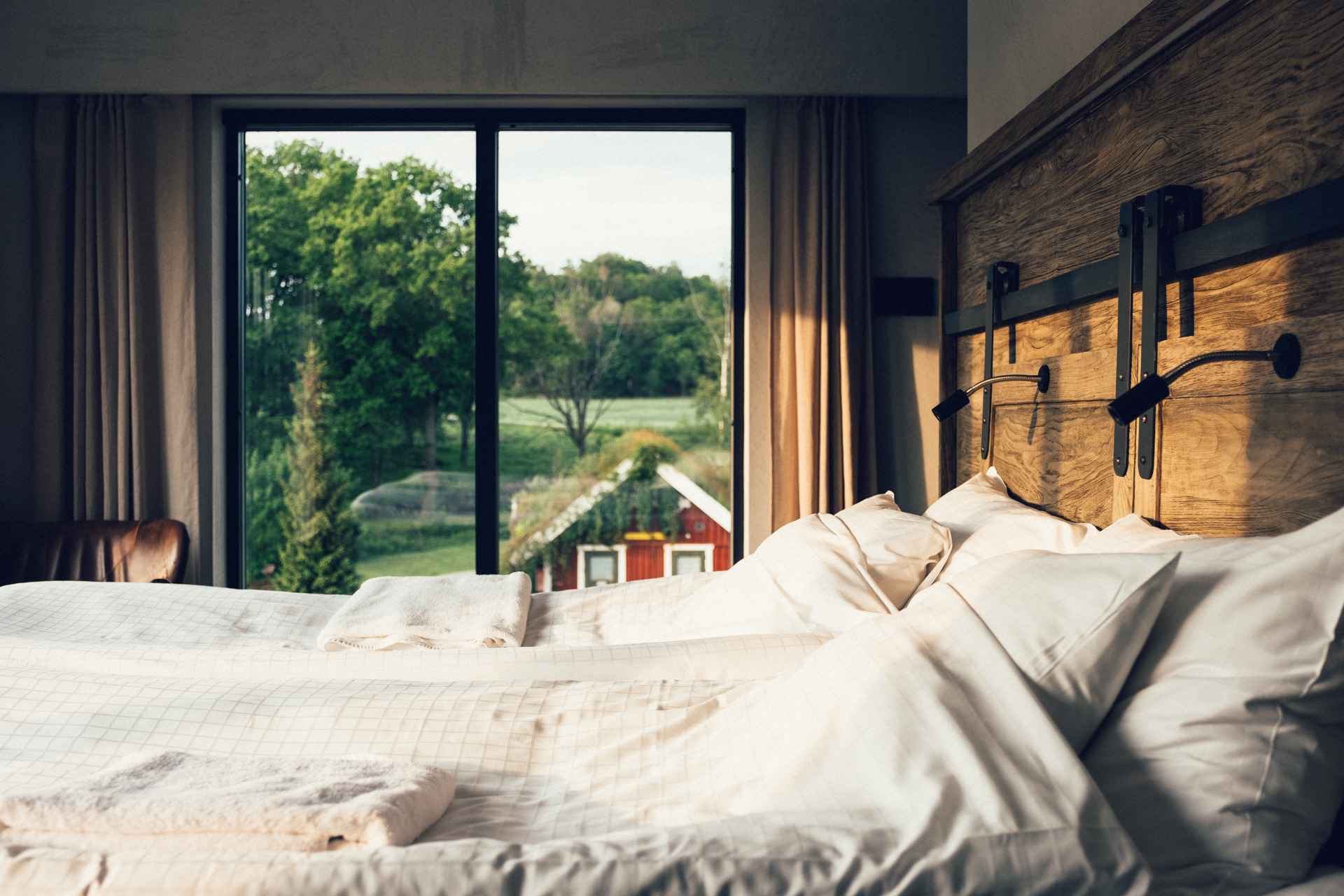 A double bed in a hotel room with windows that look out to a red cabin and a forest.