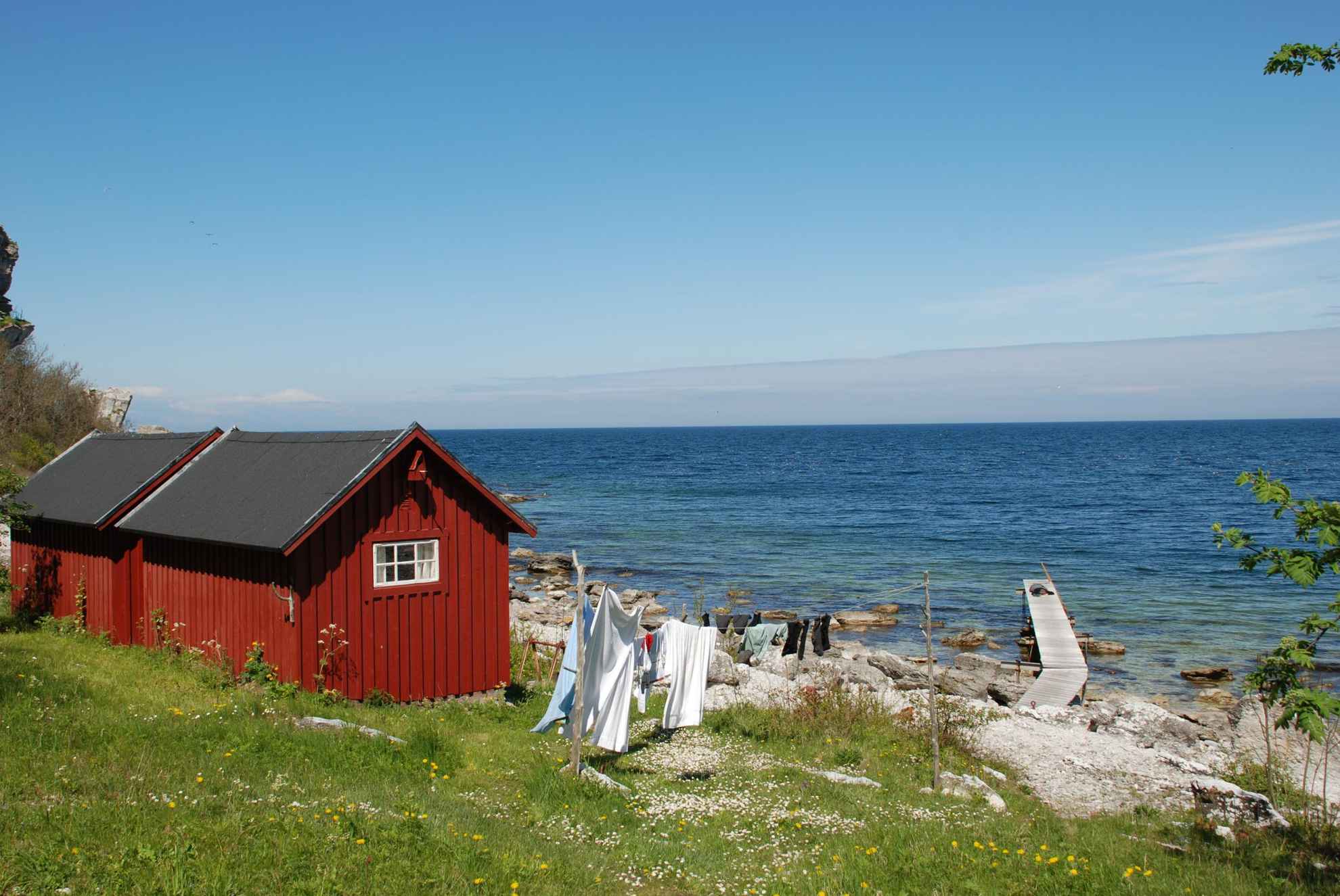 A red wooden cottage next to the water during summer.
