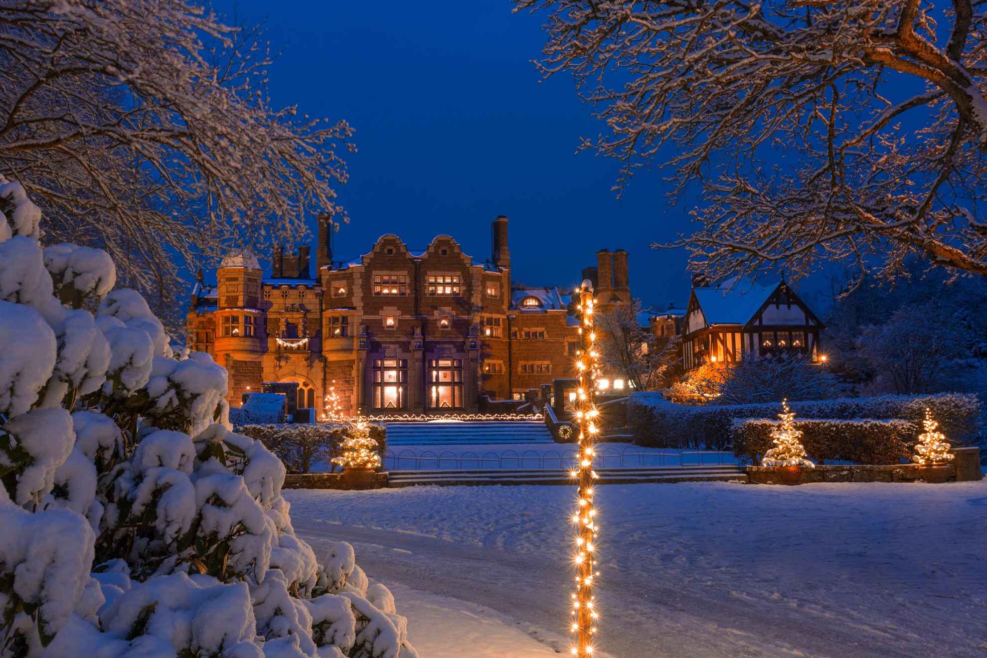A castle covered in snow and Christmas lights at dusk.