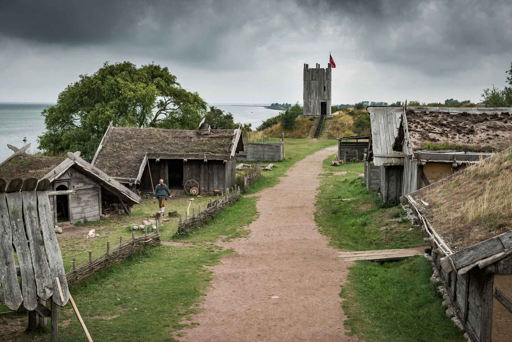 A gravel road leading through a traditional viking village with wooden houses with grass-covered roofs.