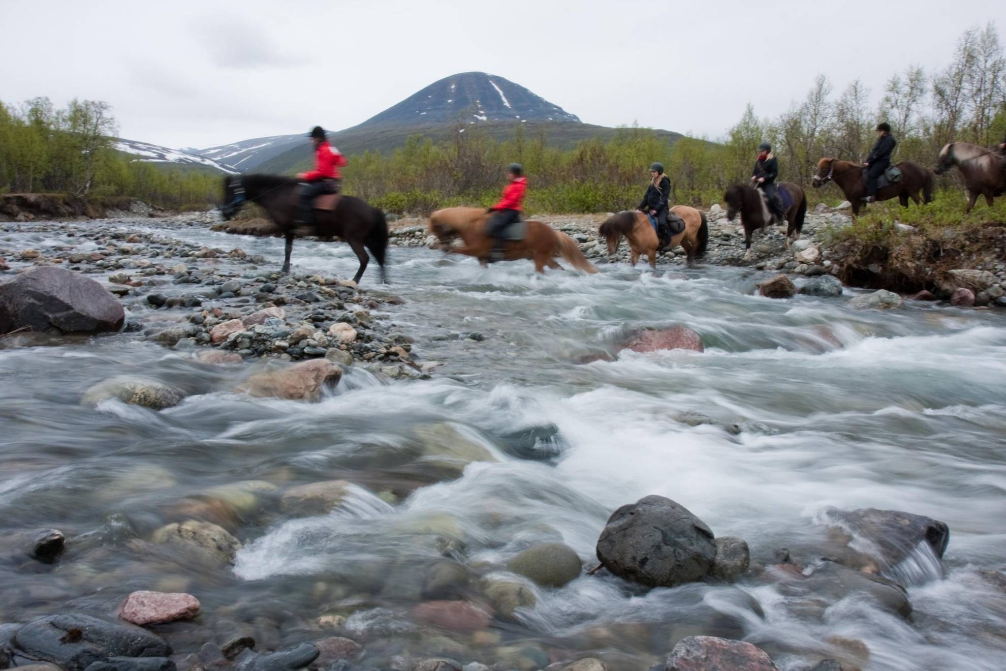 People on horseback cross a stream in Swedish Lapland.
