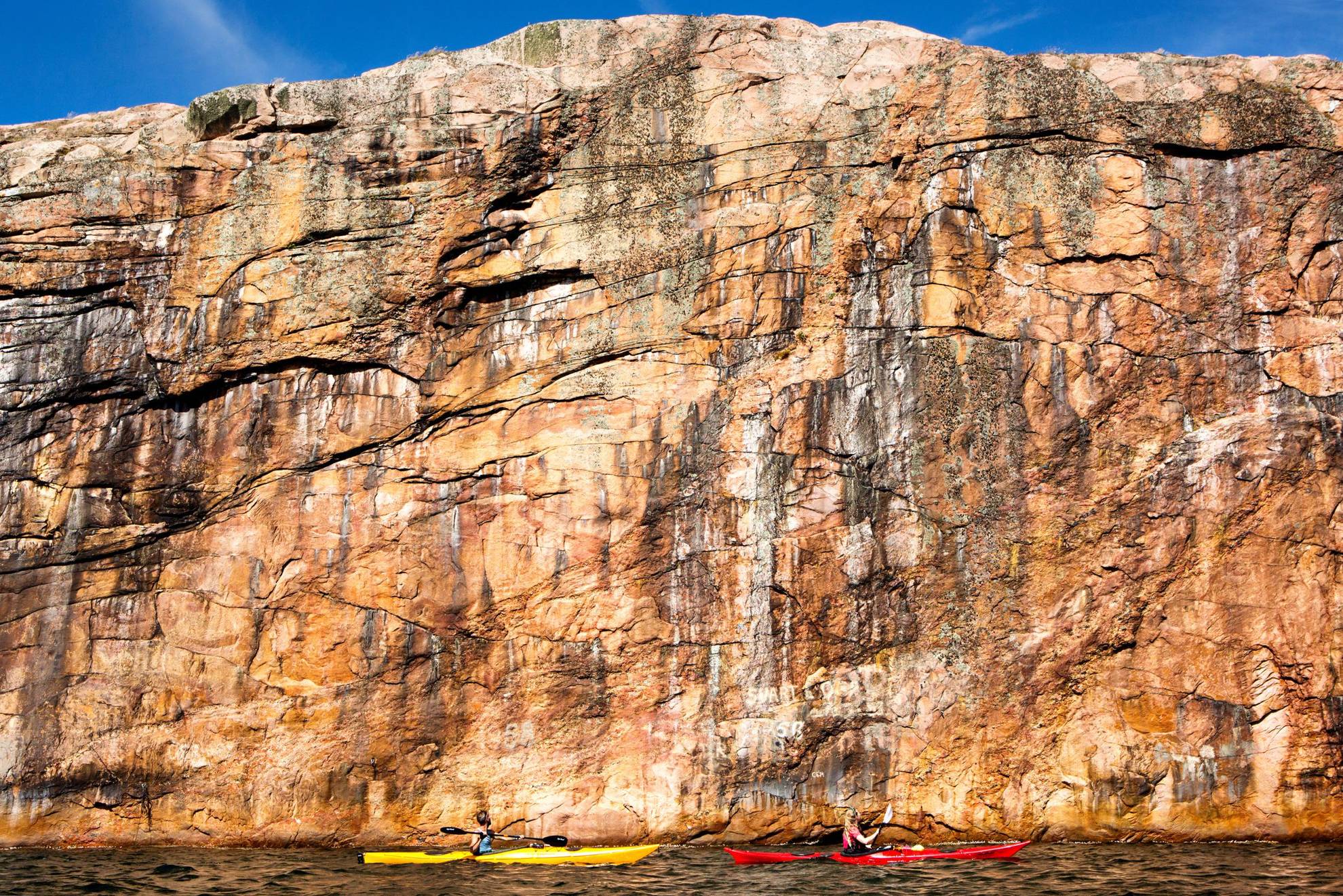 Two people kayaking by a steep cliff.