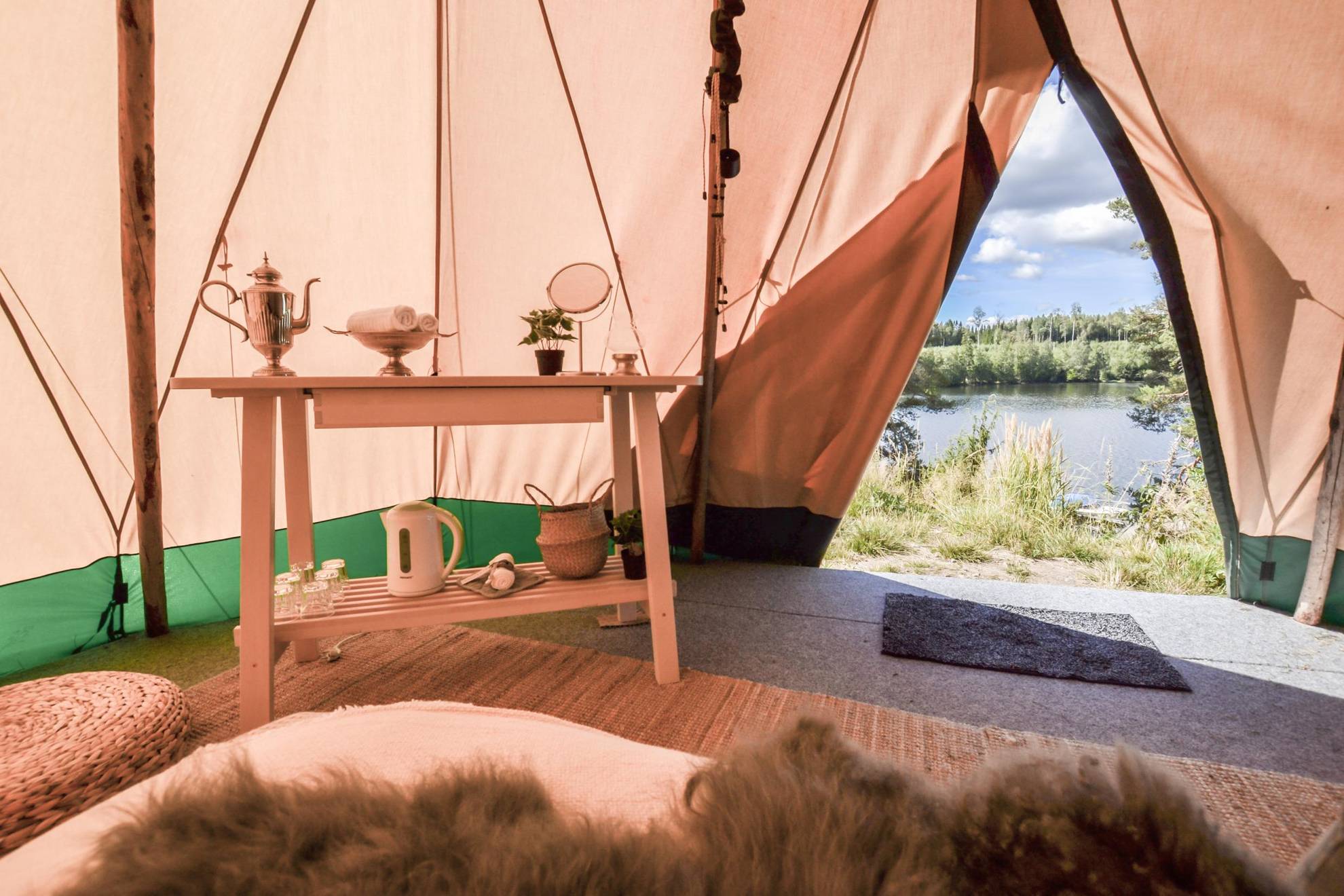A view from inside a tipi tent. A forest and a lake can be seen outside.