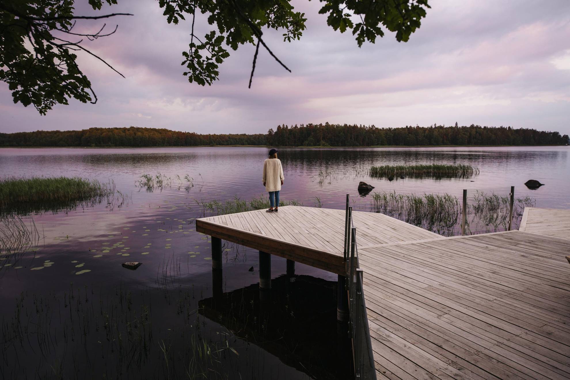 A woman is standing on the edge of a jetty while enjoying the view of a lake.