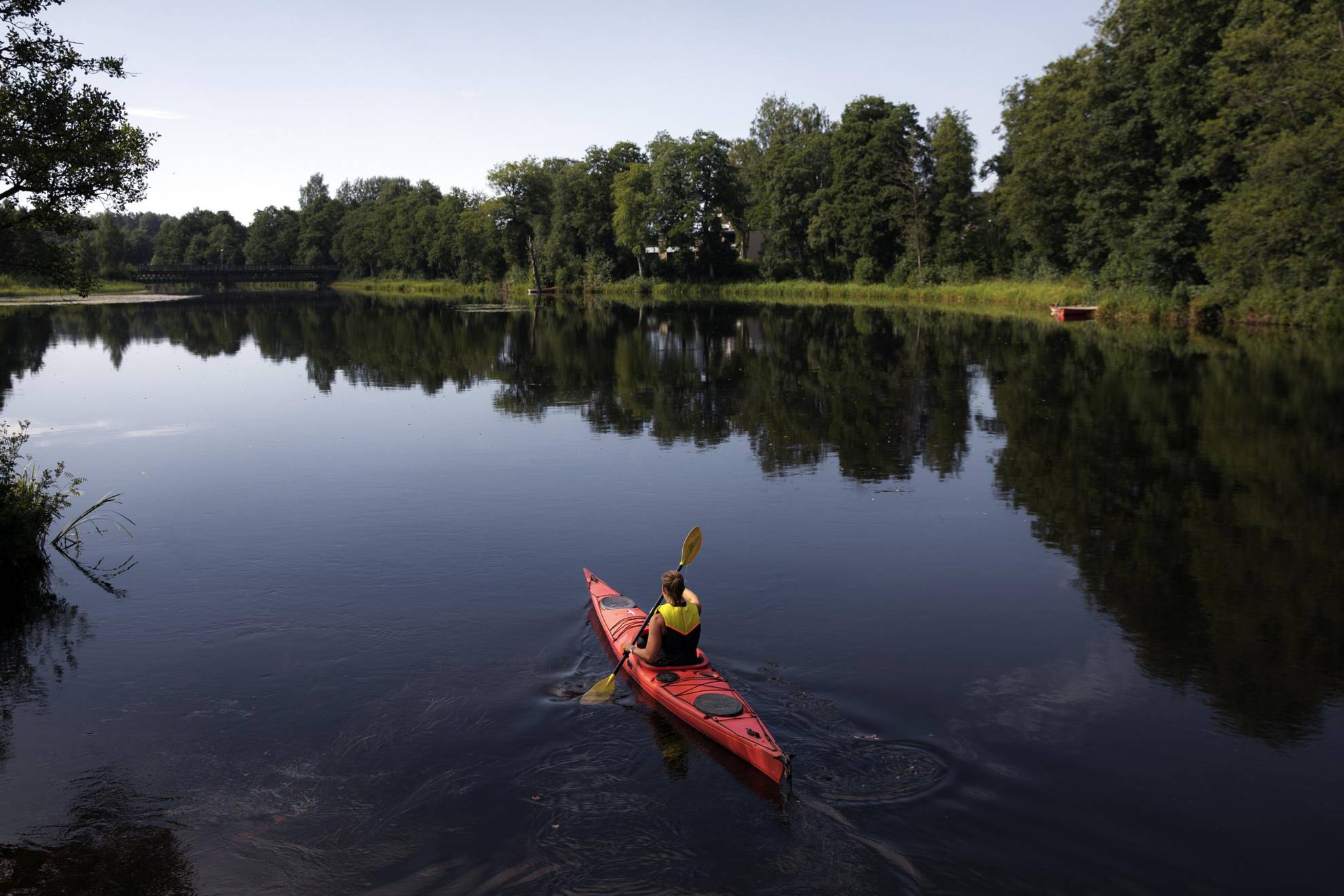 A person is kayaking on a calm lake during the summer.
