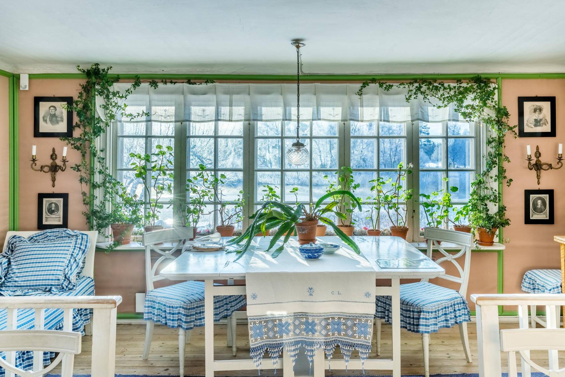 A kitchen with a large window, with lots of plants and white-and-blue fabrics.