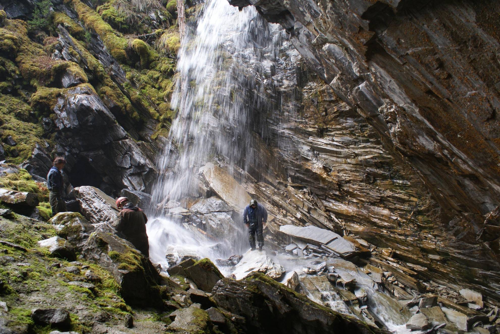 Three people standing in a glade with a waterfall. One of the people is standing in the waterfall.