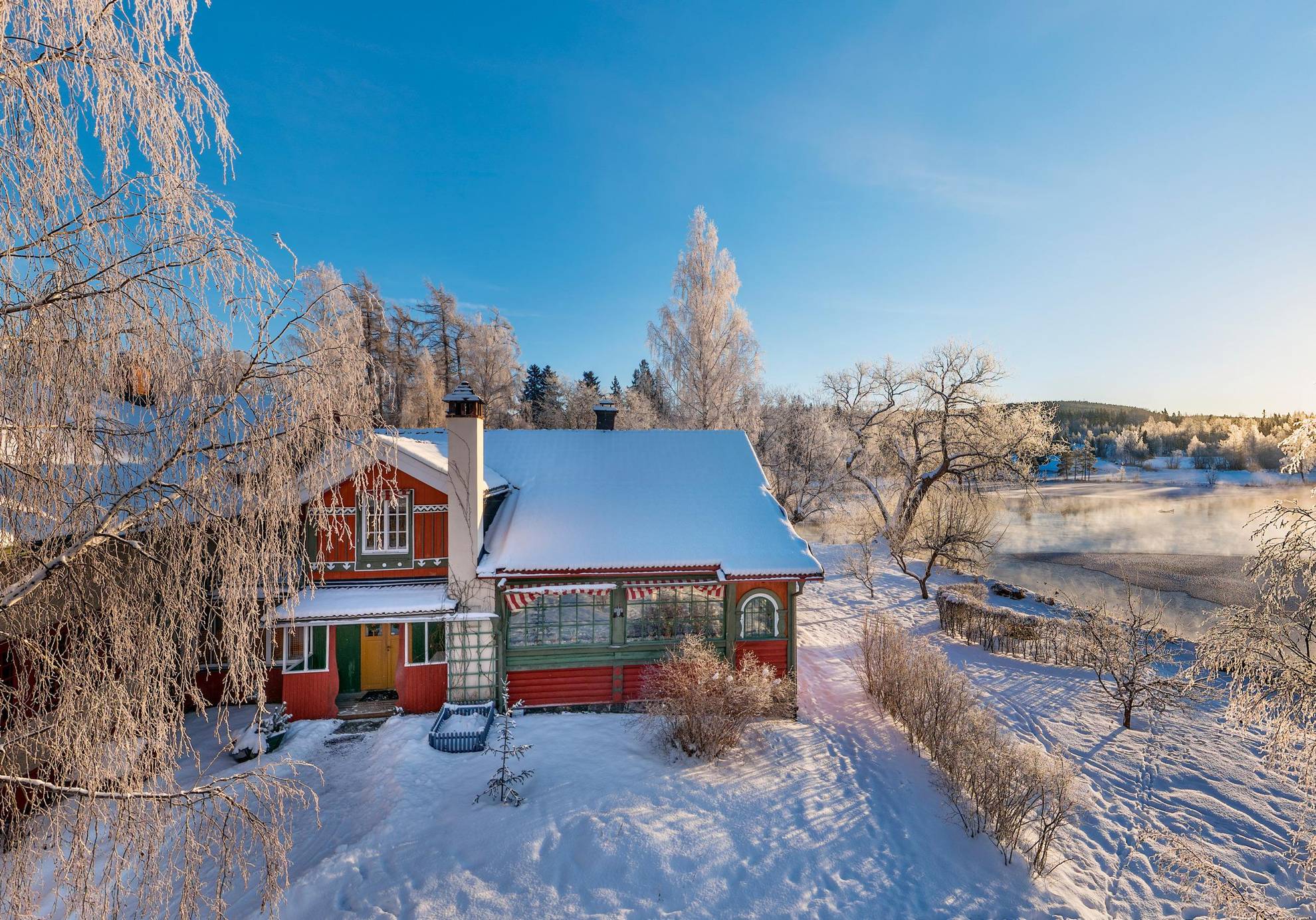 A house by the water in a frosty and snowy winter landscape. A lake is in the background.