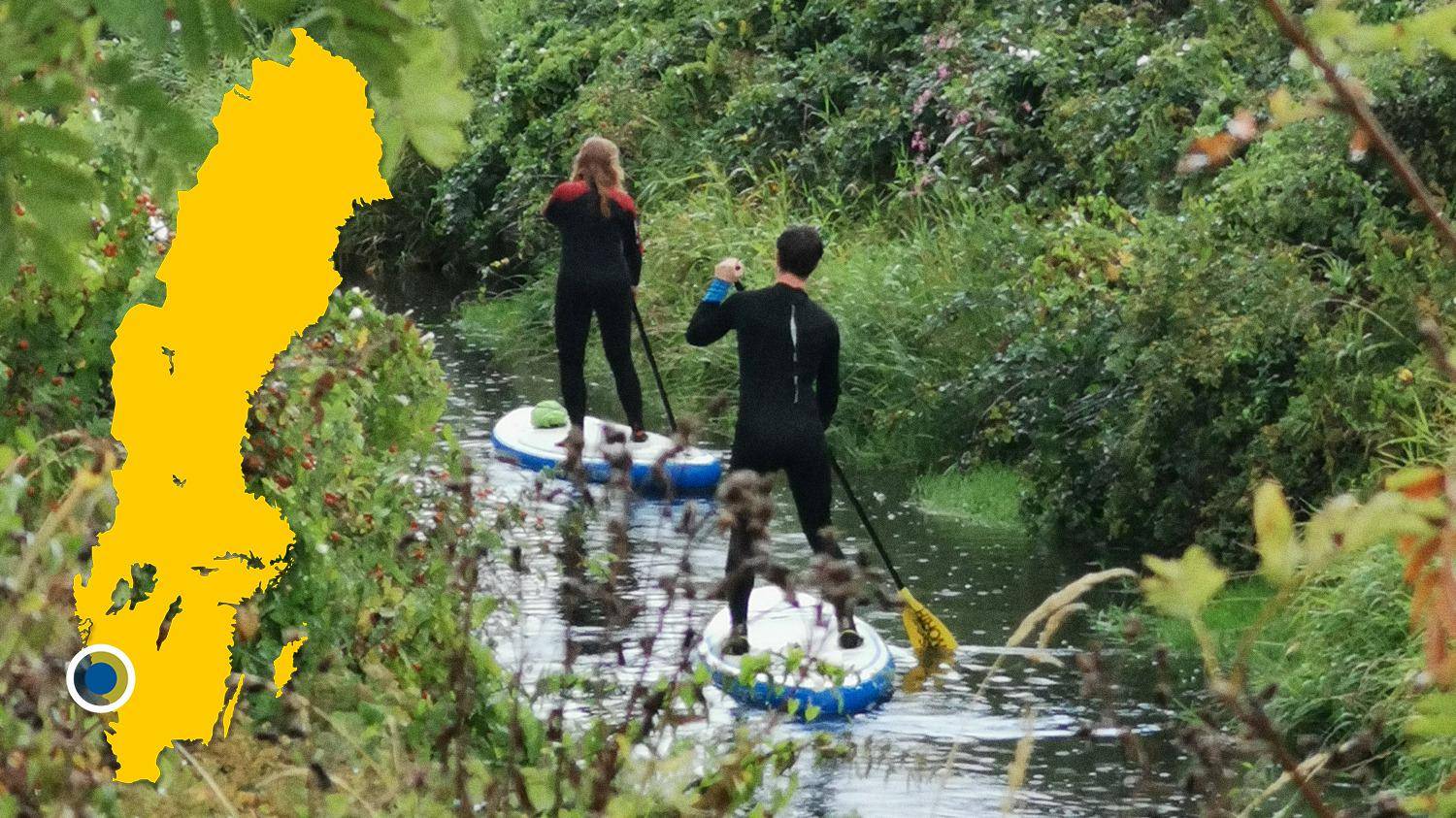 Two people paddle on stand up paddleboards in a river. There is a yellow map of Sweden with a mark that locates Himleån.