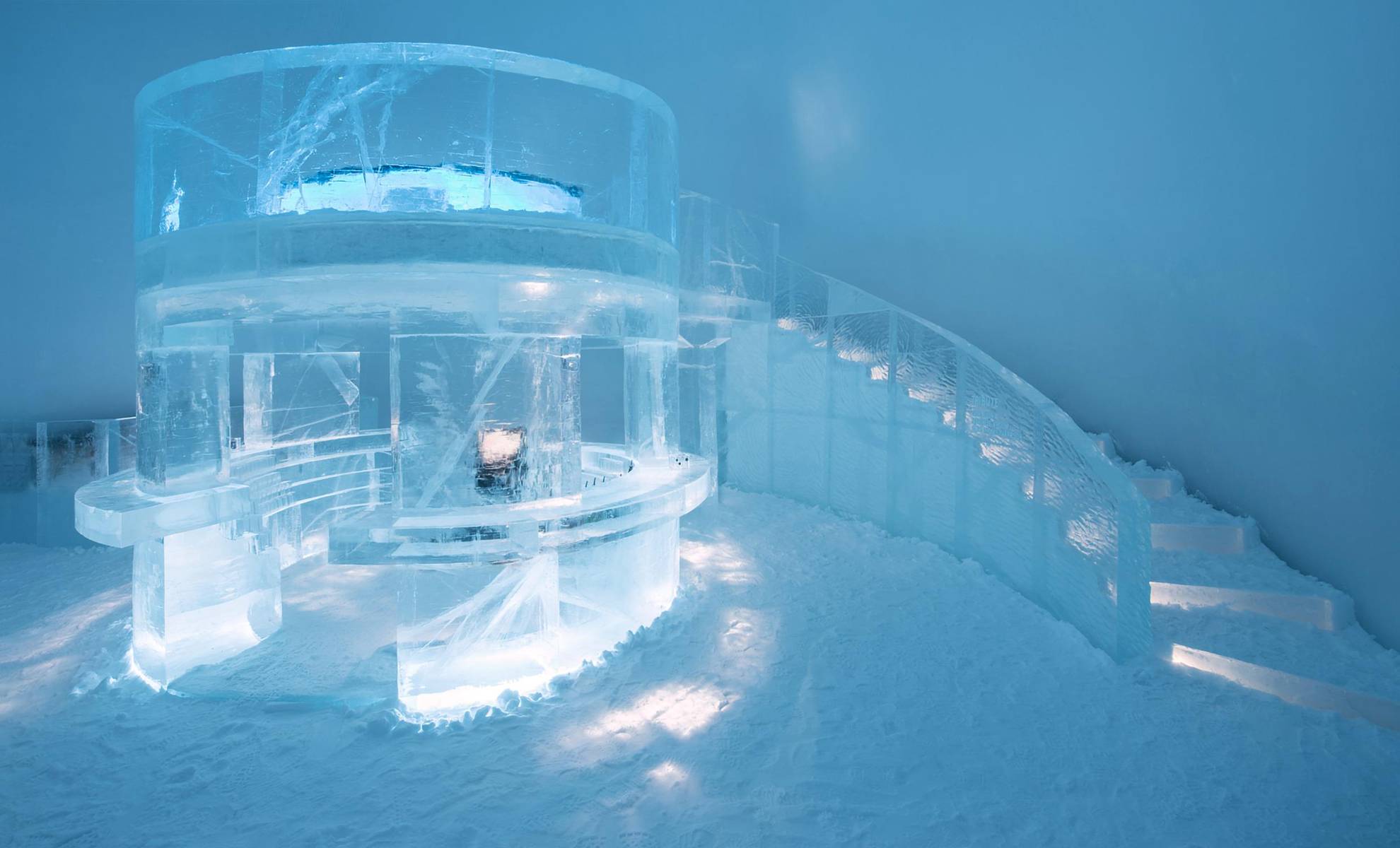 A bar made out of ice in a room made out of ice, with stairs at the back.